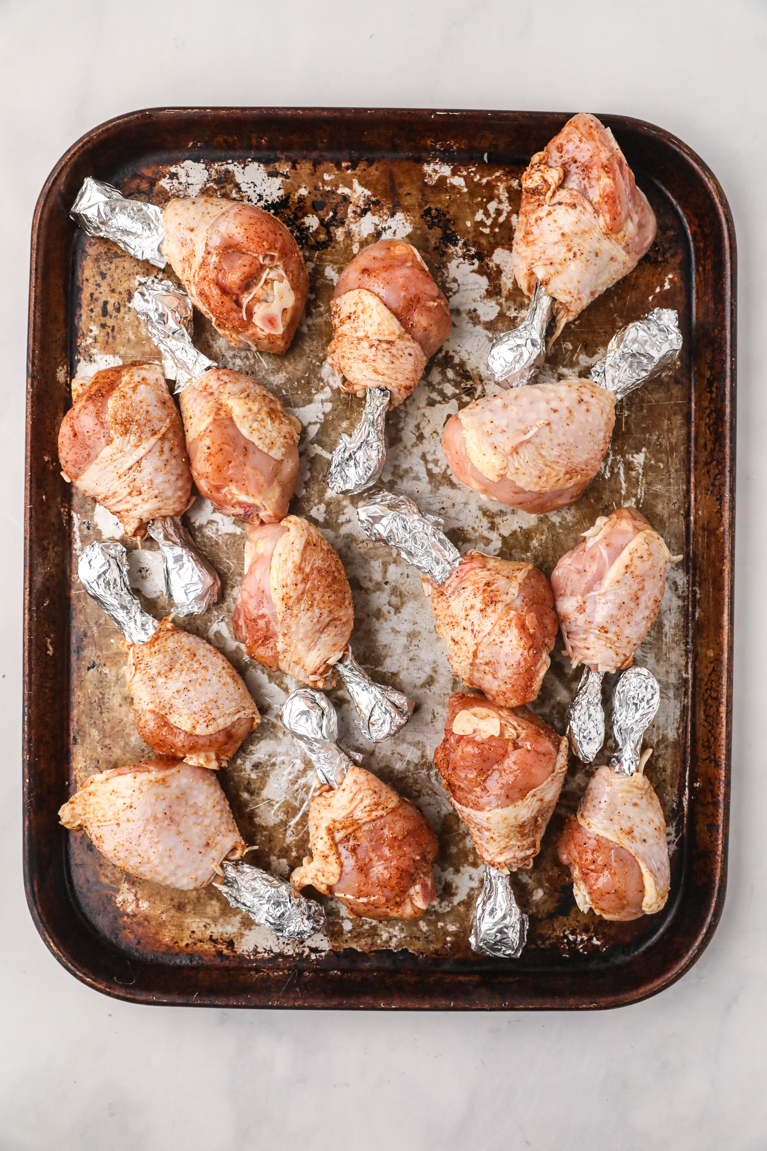 Seasoned chicken drumsticks on a baking sheet with the bone ends wrapped in aluminum foil.