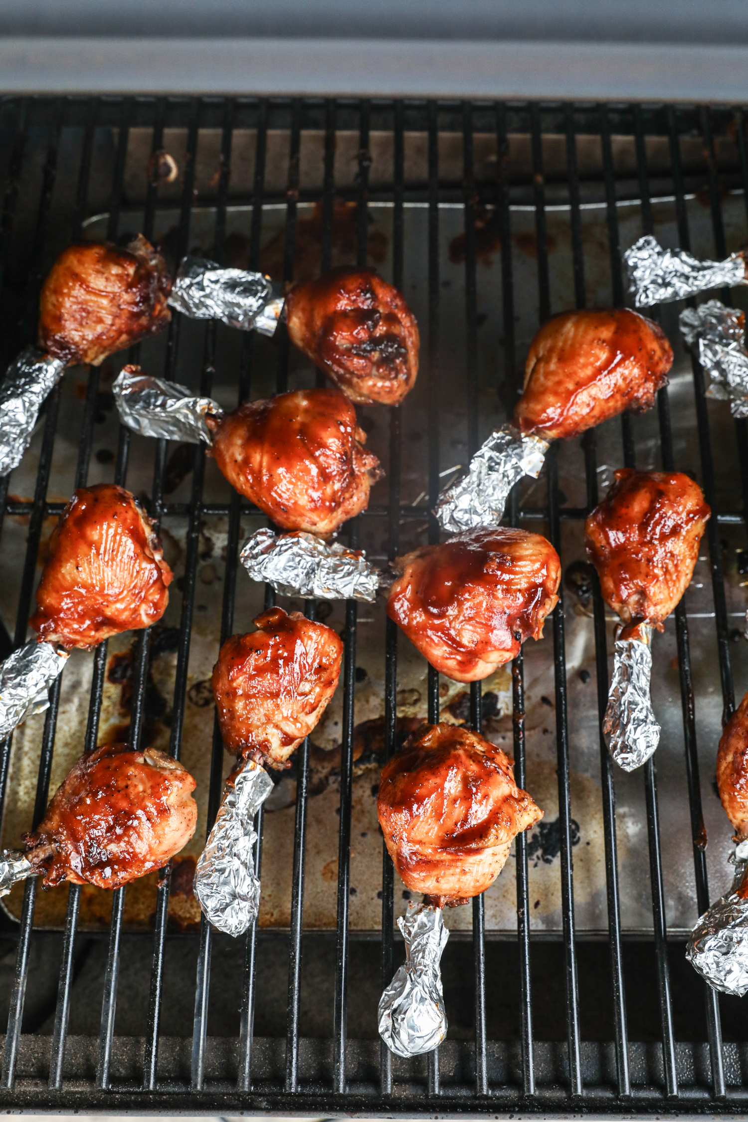Chicken drumsticks on the smoker, now darkened and glossy from the BBQ sauce glaze.