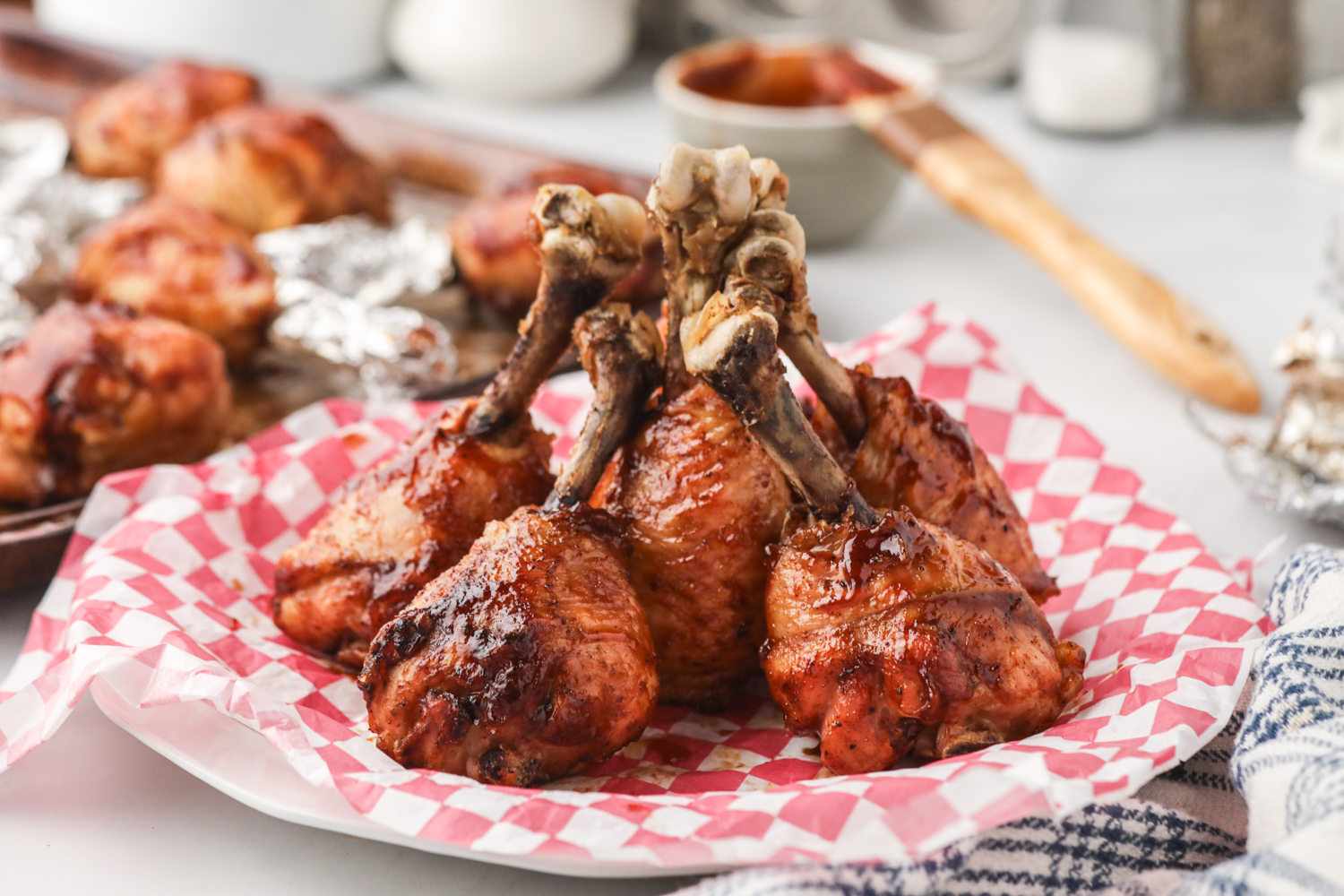 A plate of smoked chicken lollipops stacked upright on a red and white checkered paper, ready to serve.