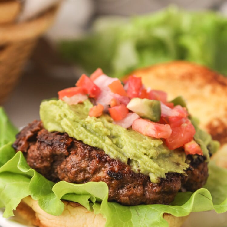 Close-up of a taco burger with a thick patty, fresh lettuce, guacamole, and vibrant pico de gallo.