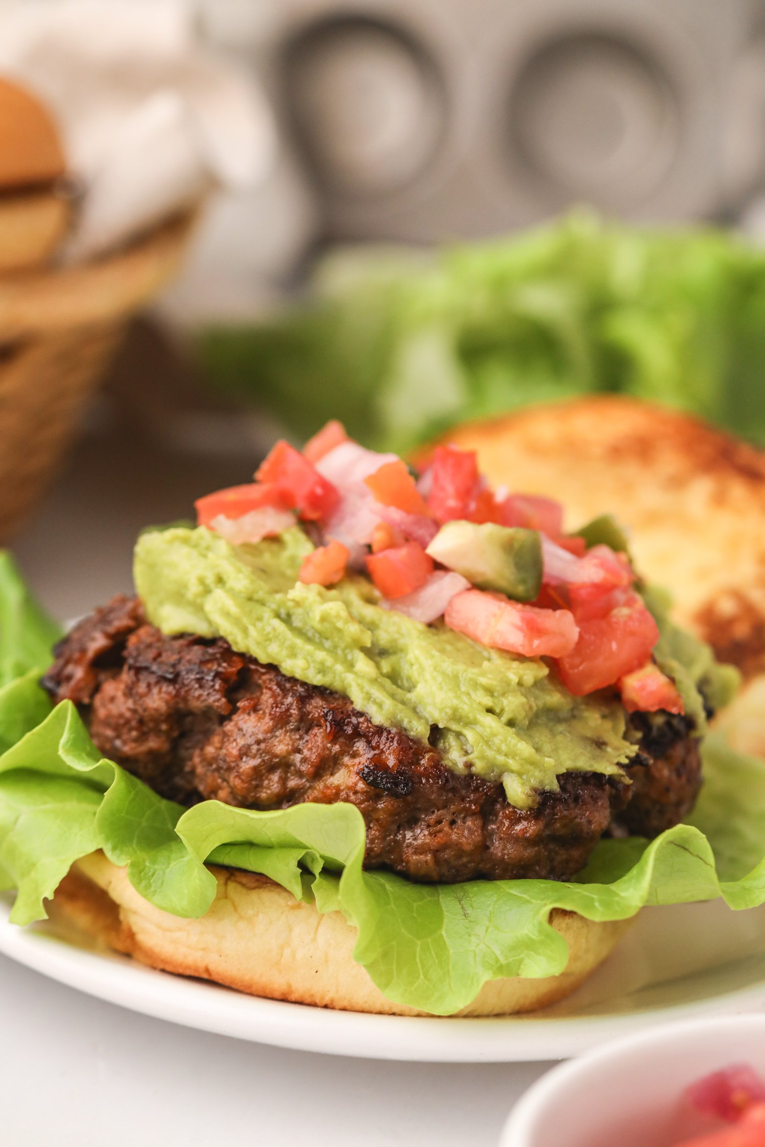 Close-up of a taco burger with a thick patty, fresh lettuce, guacamole, and vibrant pico de gallo.
