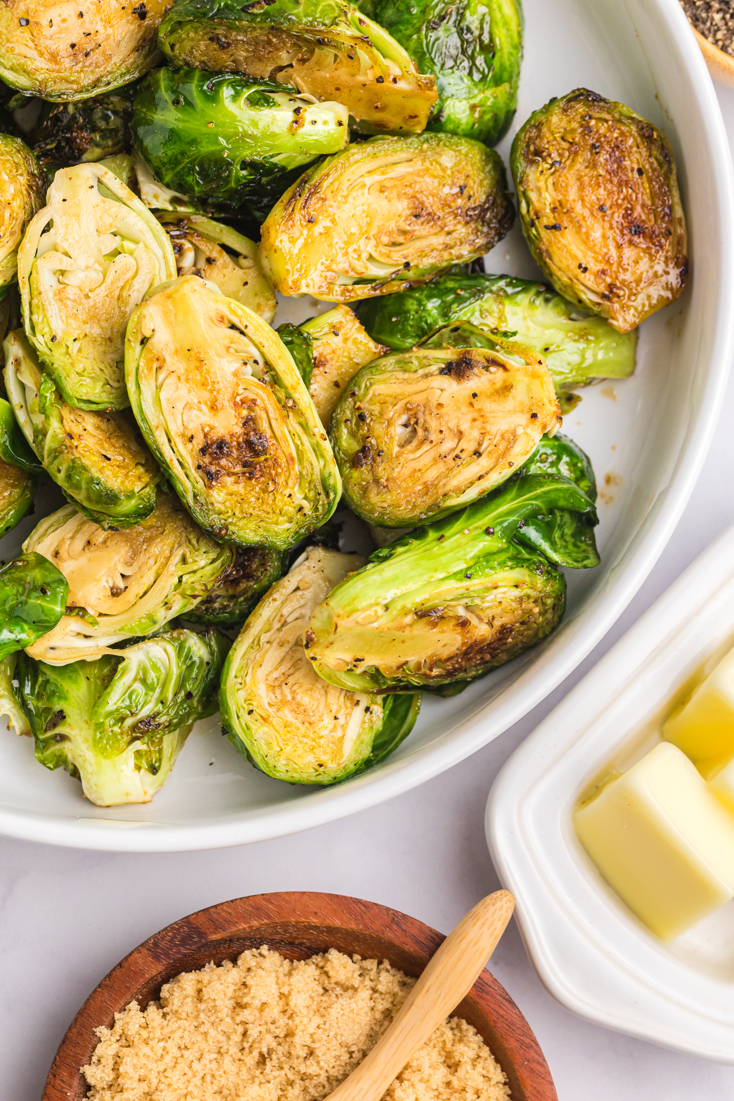 Golden-brown Brussels sprouts in a serving bowl with a dish of butter and brown sugar on the side.