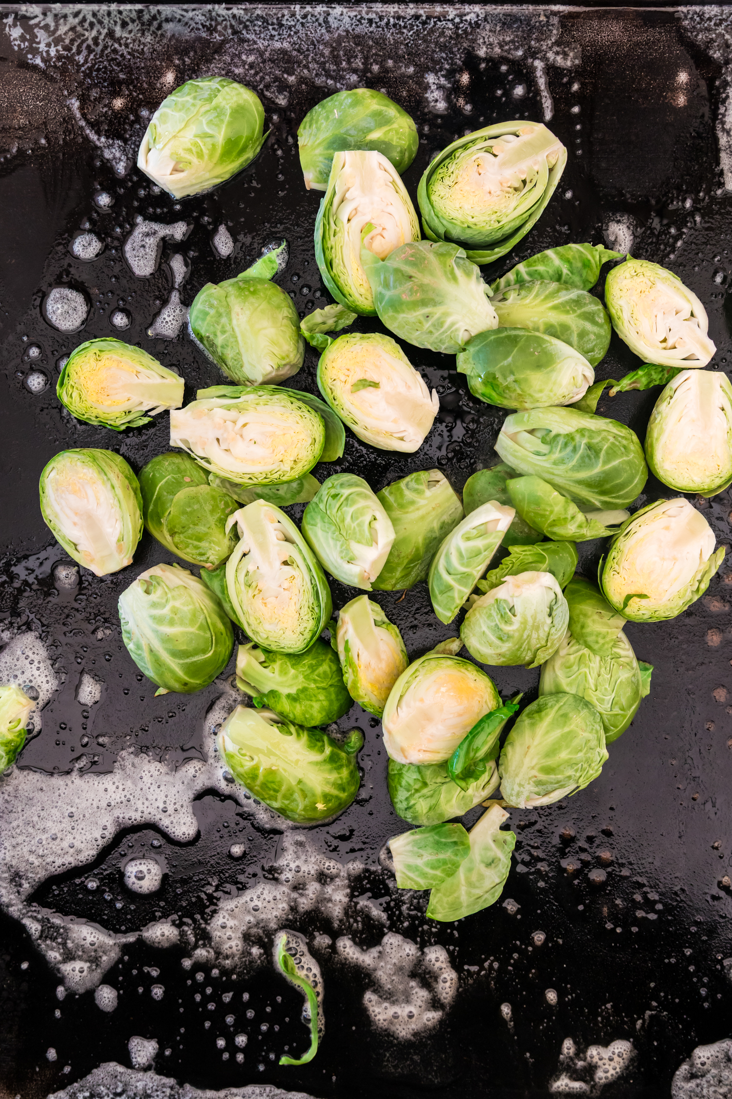 Halved Brussels sprouts placed on a hot griddle surface, beginning to cook in melted butter.