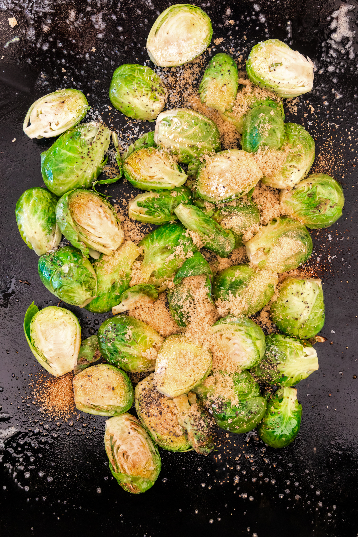 Brussels sprouts on a griddle sprinkled with brown sugar, salt, and black pepper for seasoning.