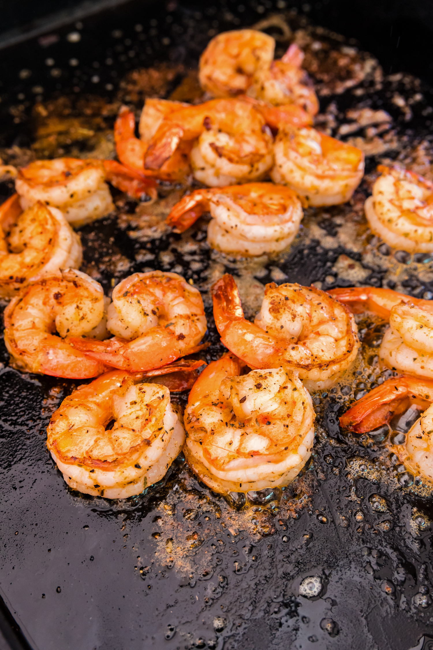 Close-up of shrimp on a flat-top griddle, fully cooked to a golden brown with slightly curled edges.