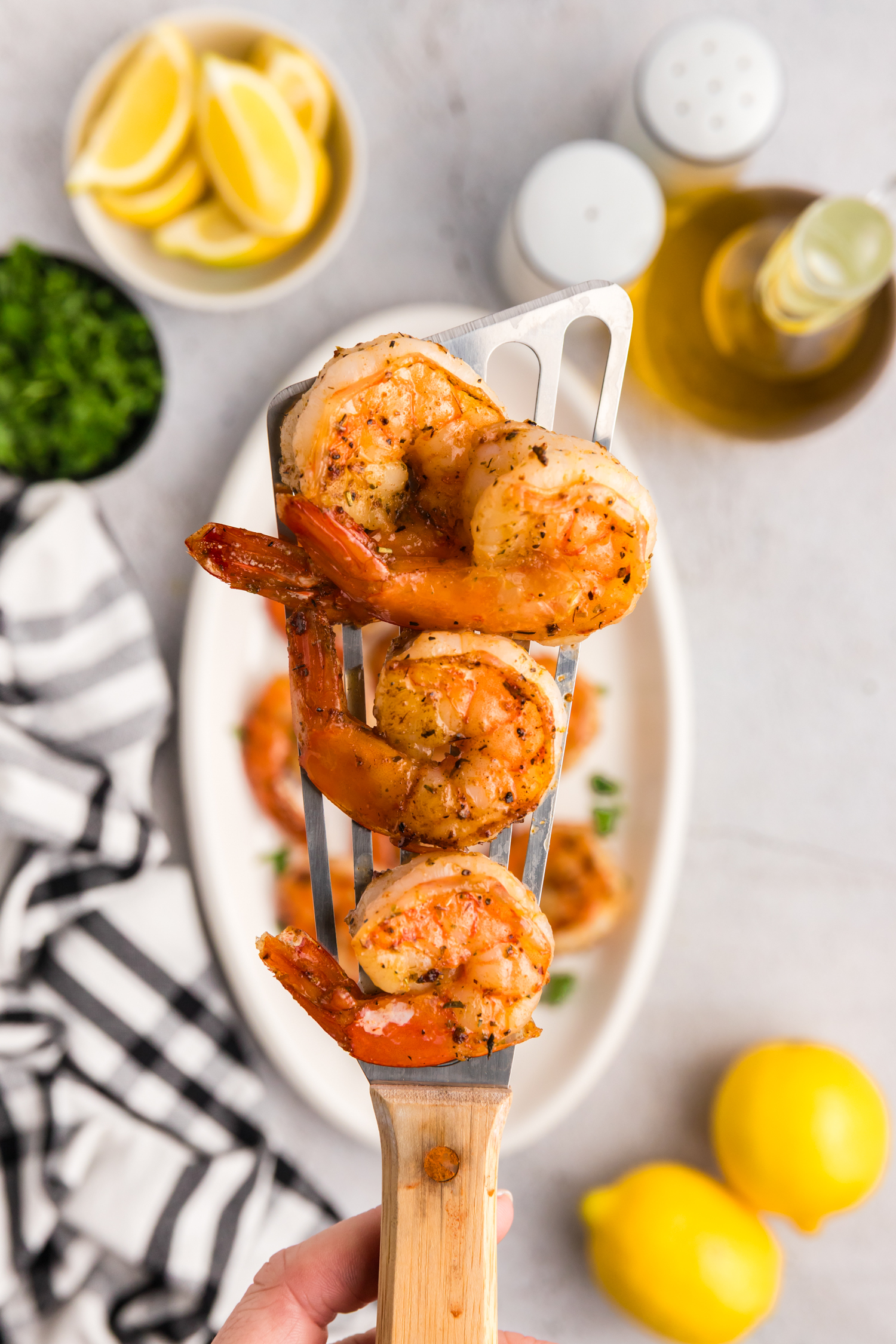Cooked shrimp resting on a metal spatula held above a serving plate with parsley garnish.