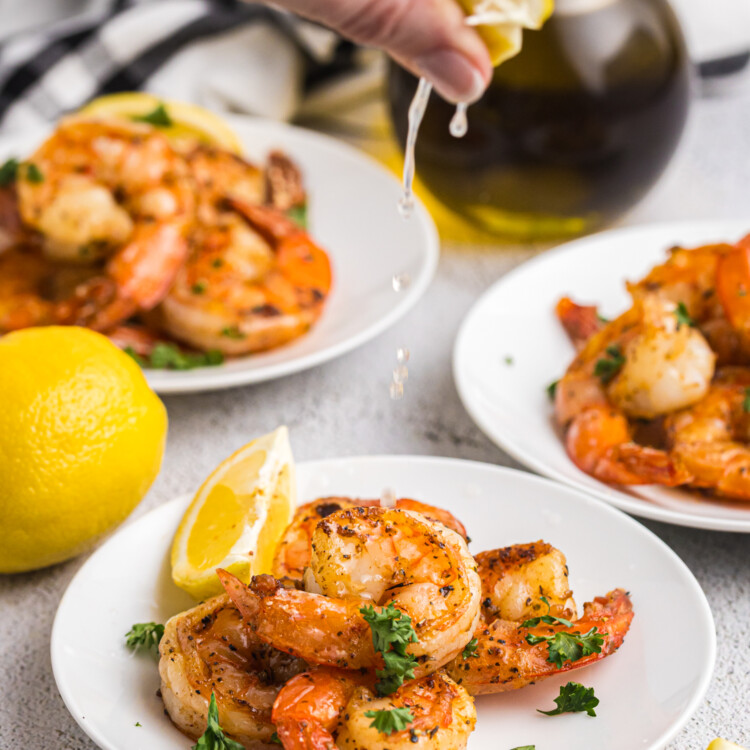 A hand squeezing fresh lemon juice over a plate of seasoned, grilled shrimp.
