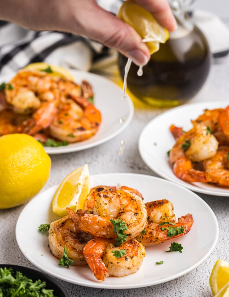 A hand squeezing fresh lemon juice over a plate of seasoned, grilled shrimp.