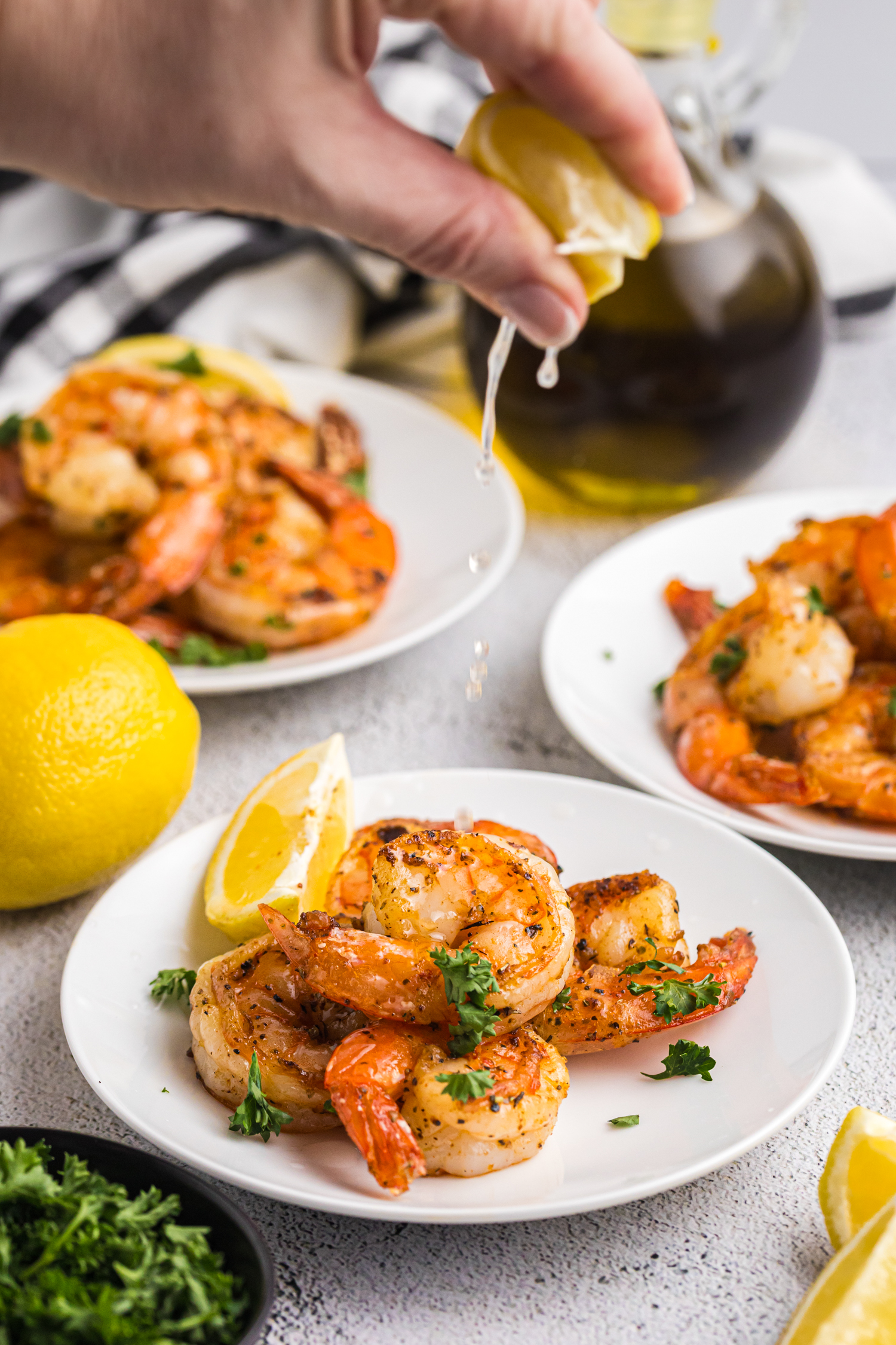 A hand squeezing fresh lemon juice over a plate of seasoned, grilled shrimp.

