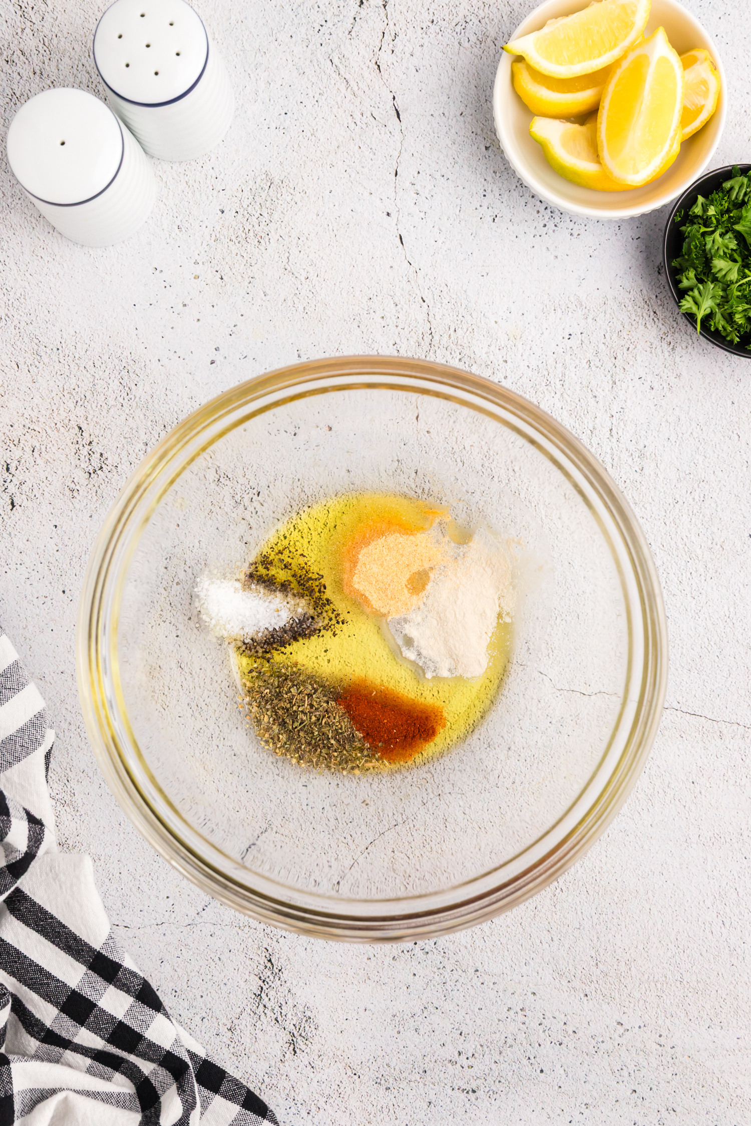 A glass bowl containing olive oil and a variety of seasonings, including paprika, salt, pepper, garlic powder, and herbs.
