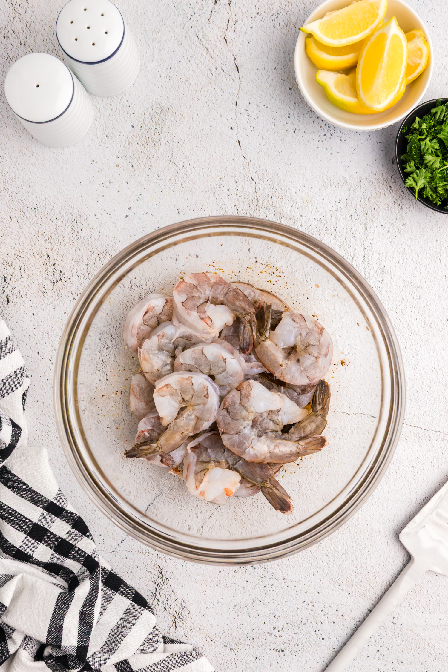 Raw shrimp added to a bowl with marinade at the bottom, about to be mixed.