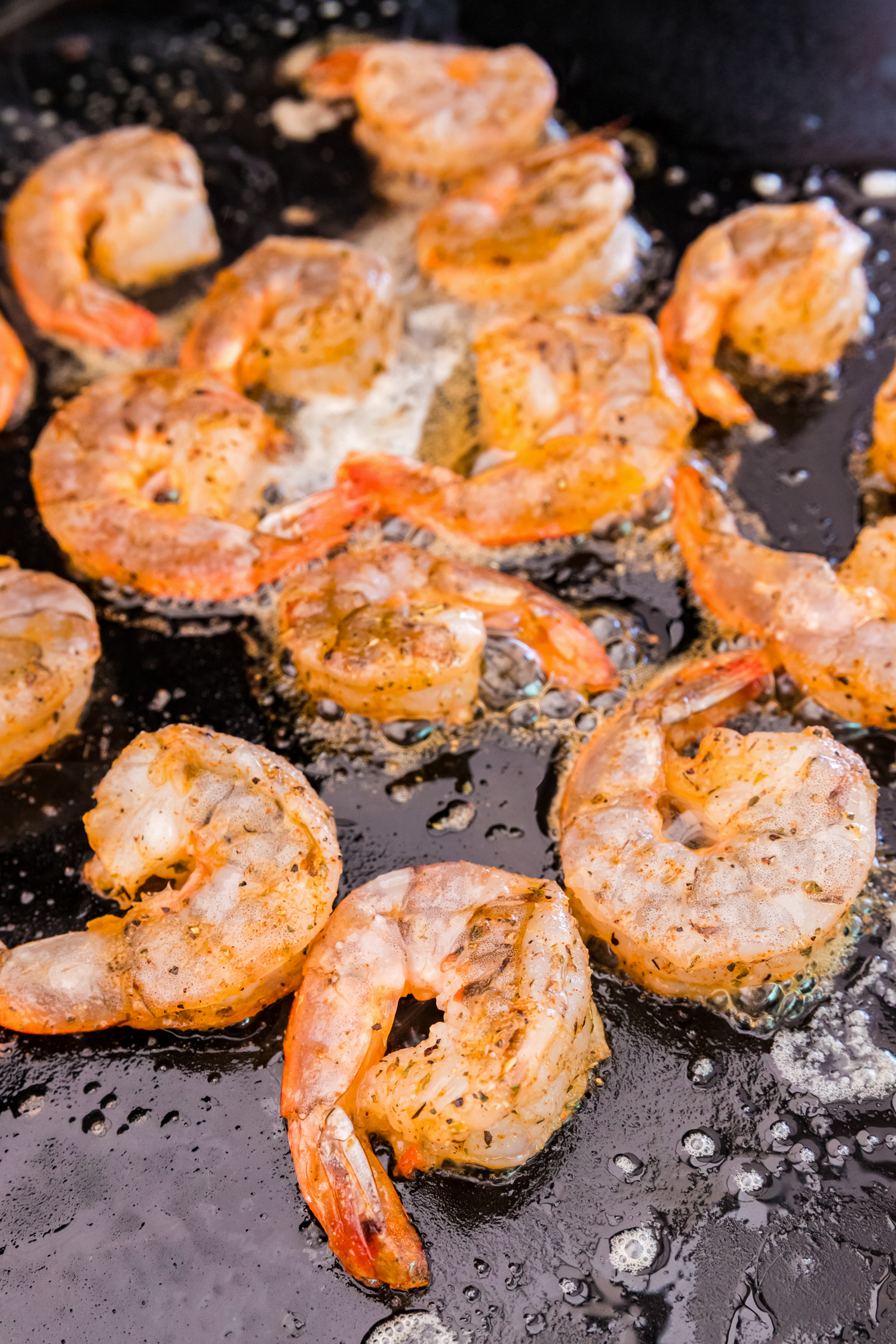Shrimp sizzling on a hot griddle in melted butter, beginning to cook.