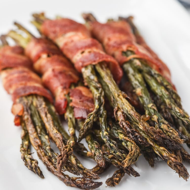 Final presentation of bacon-wrapped asparagus served on a white plate, with a focus on the crispy bacon and roasted asparagus tips.