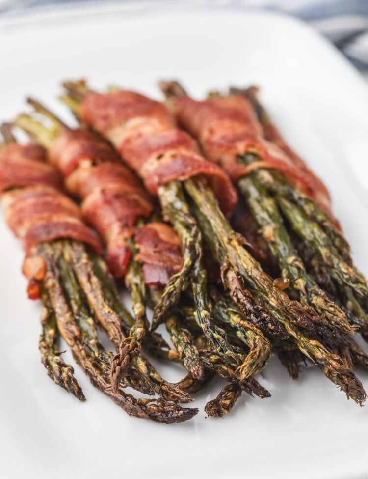 Final presentation of bacon-wrapped asparagus served on a white plate, with a focus on the crispy bacon and roasted asparagus tips.