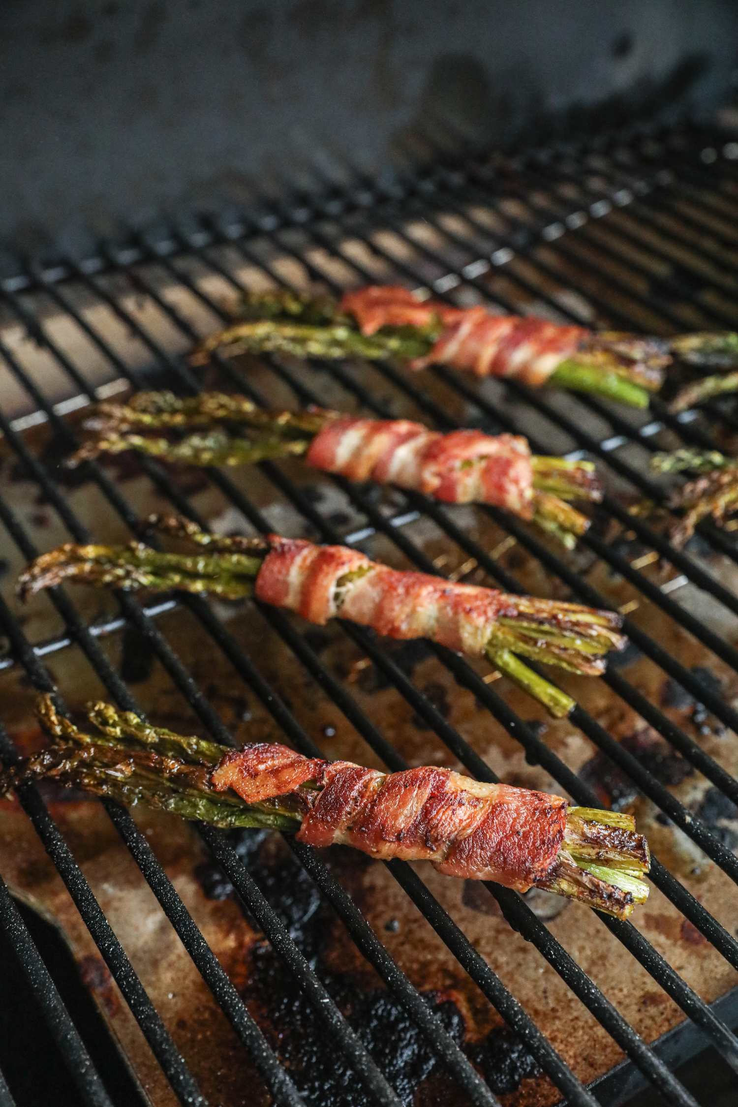 Bacon-wrapped asparagus bundles grilling, with the bacon starting to crisp and brown, and asparagus charring slightly.