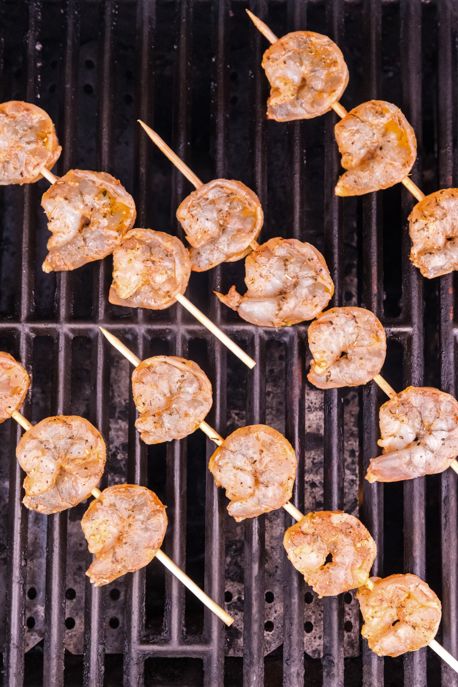 Skewered raw shrimp placed diagonally across a hot grill, beginning the cooking process.