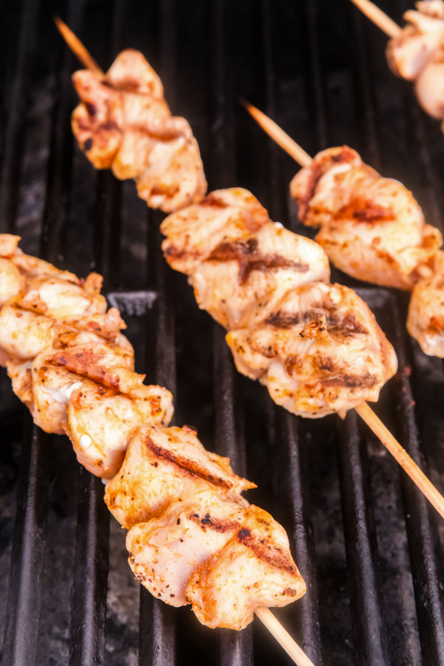 Chicken skewers on a grill with charred marks, indicating they are halfway cooked and beginning to brown.