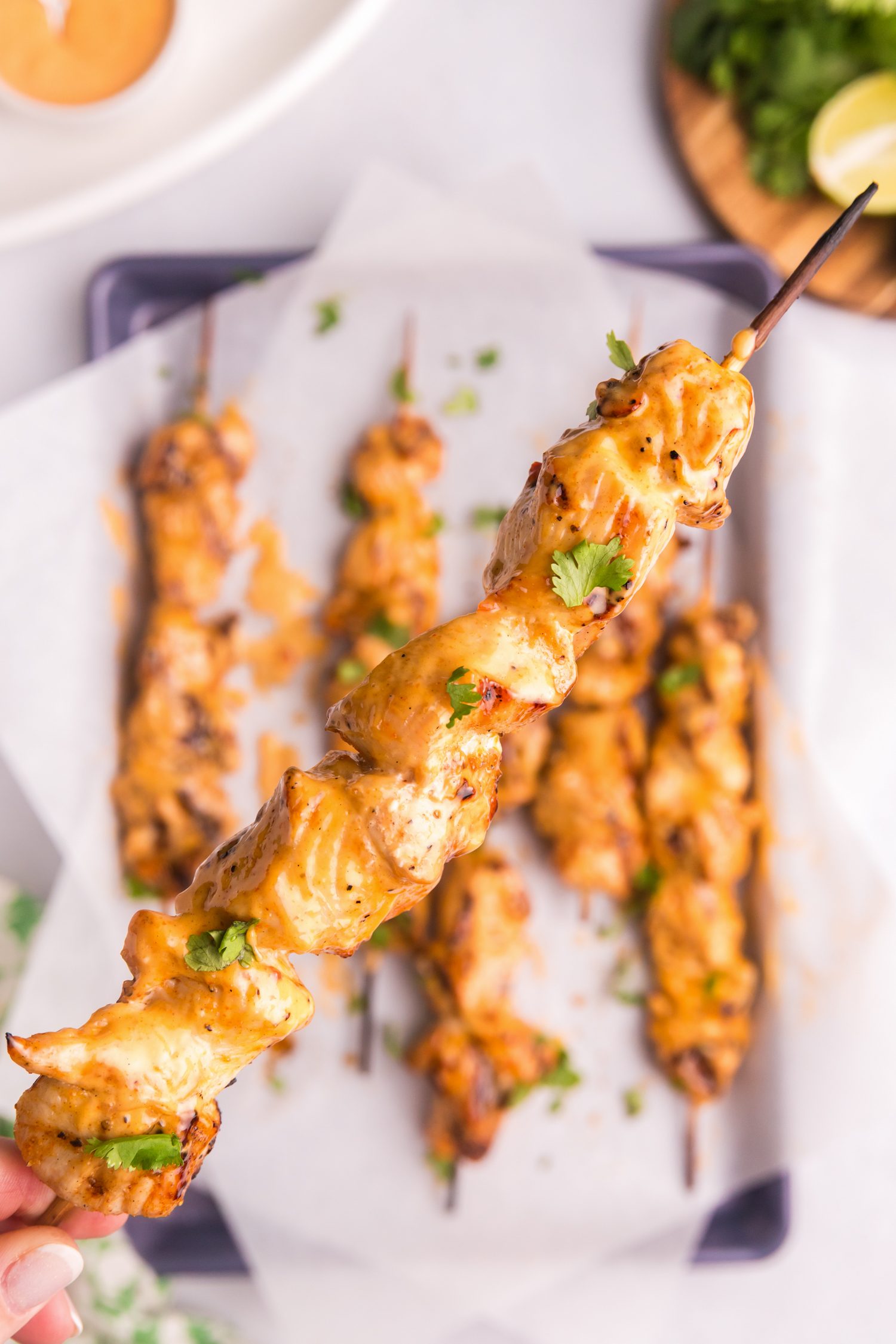 Close-up of a single Bang Bang chicken skewer being held up, showing a glossy coating of sauce and garnished with fresh cilantro.