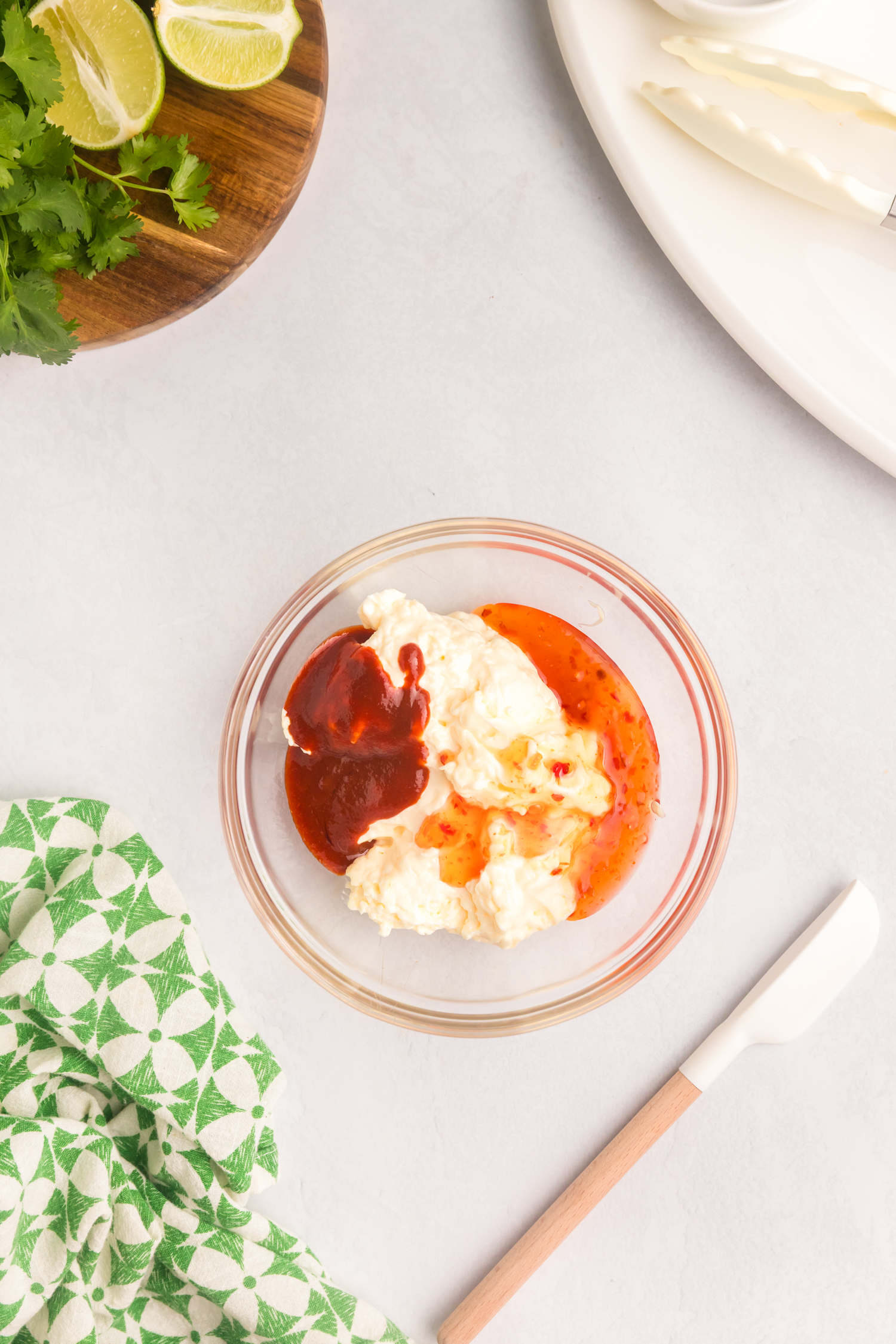 Glass bowl containing unmixed ingredients for Bang Bang sauce—mayonnaise, sweet chili sauce, and sriracha—set on a light surface.