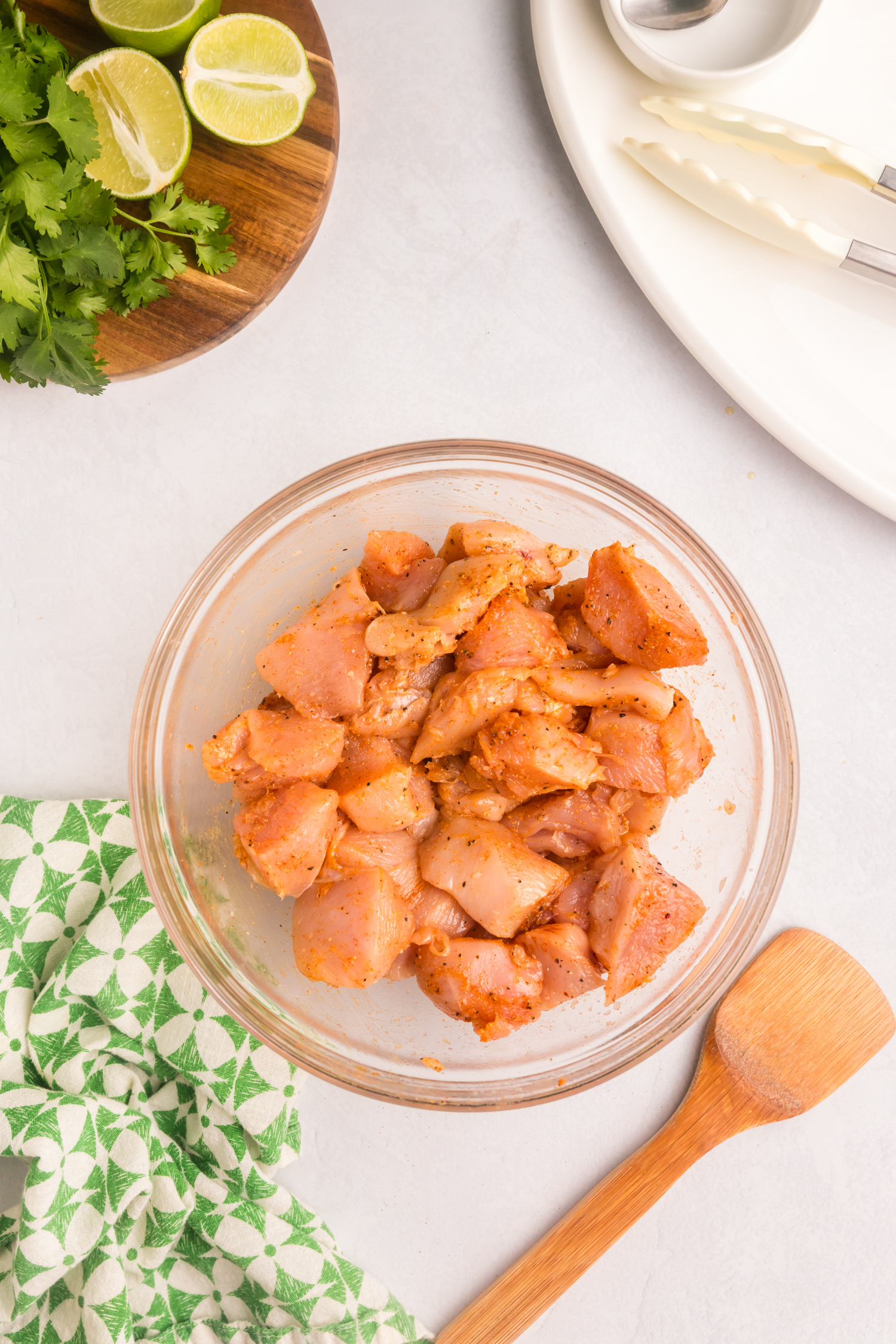 Chicken pieces thoroughly coated in marinade, evenly mixed in a glass bowl, placed beside a wooden spatula.
