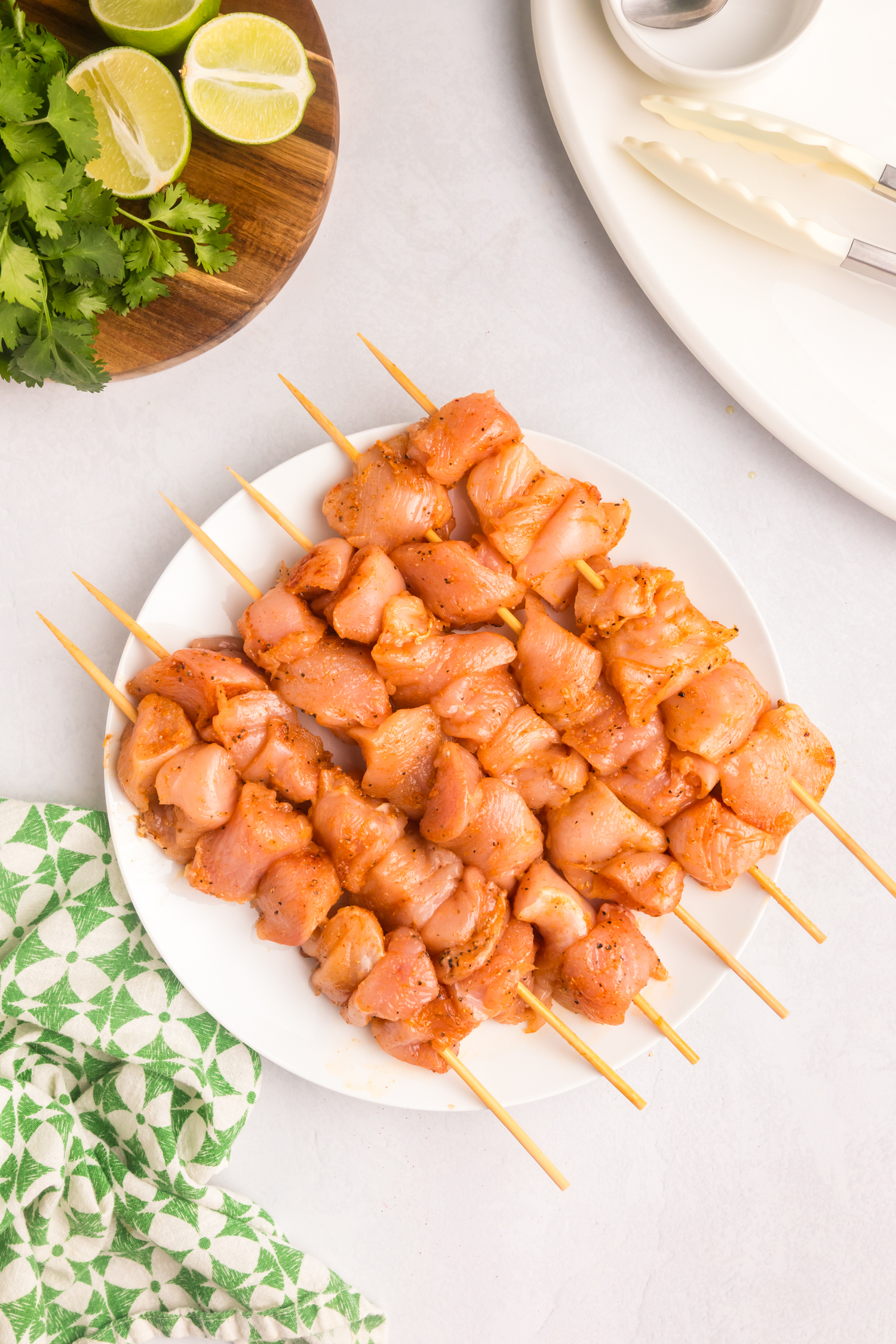 Marinated chicken pieces threaded onto bamboo skewers and neatly arranged on a white plate, ready for grilling.