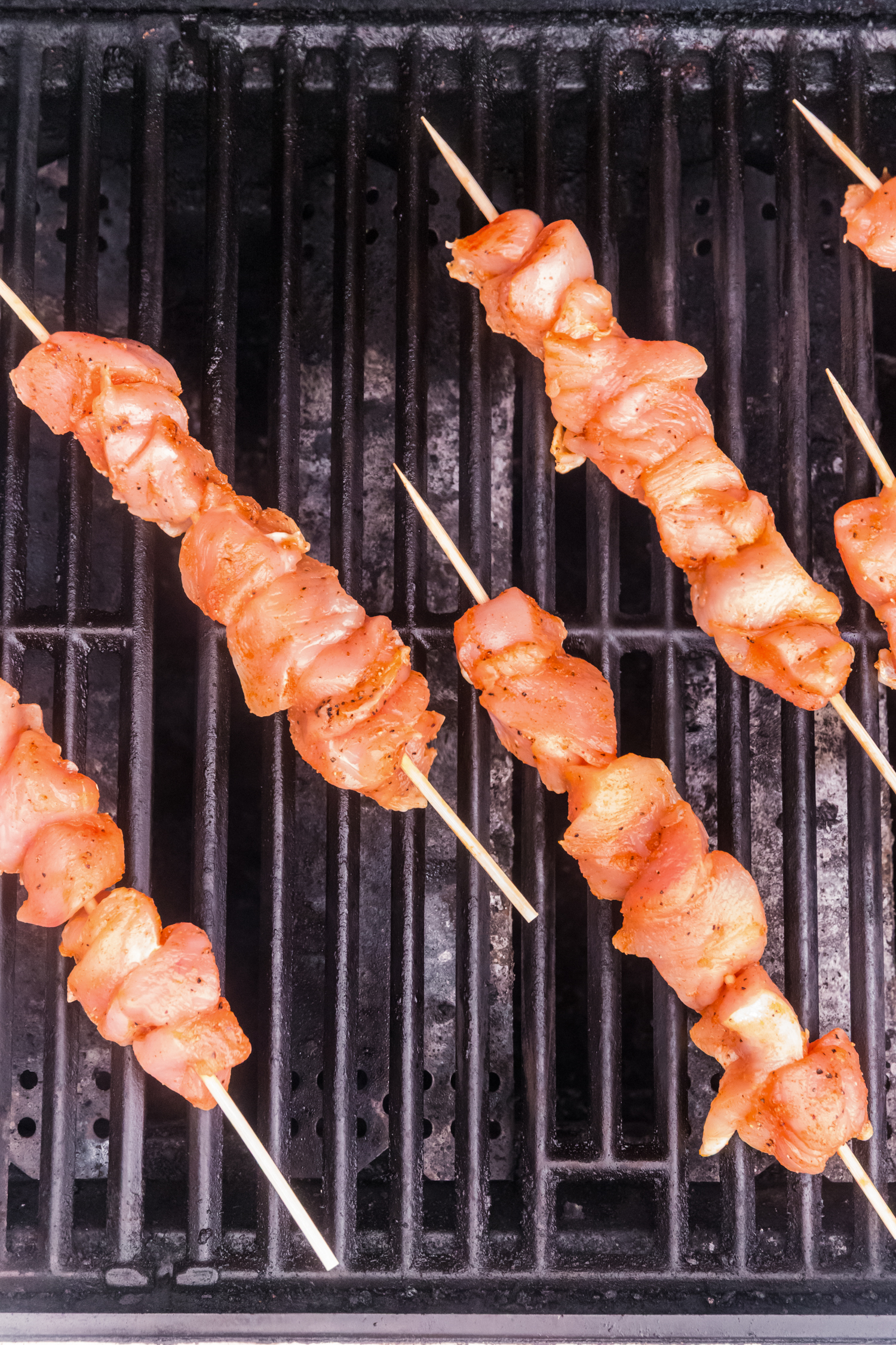 Chicken skewers cooking on a hot grill, with char marks forming as they begin to sear.