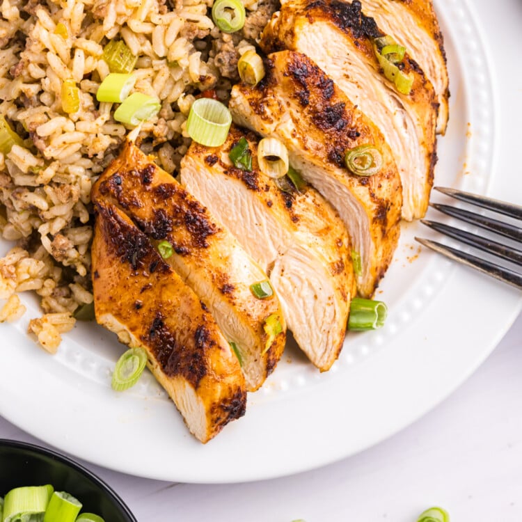 Sliced blackened chicken breast served on a plate next to a scoop of dirty rice, garnished with chopped green onions.