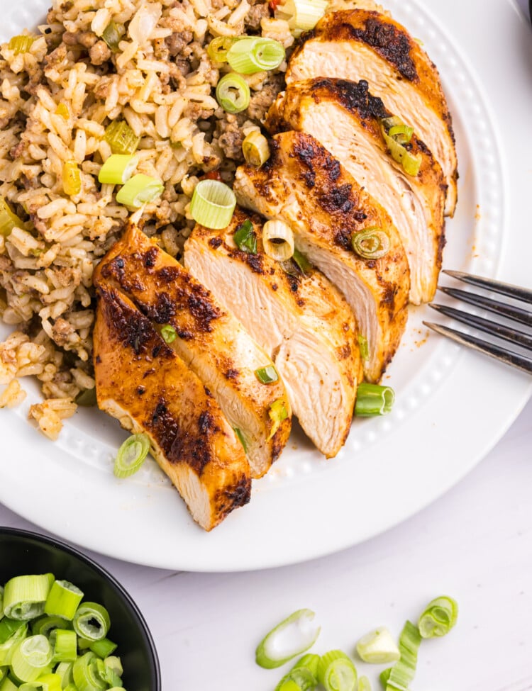 Sliced blackened chicken breast served on a plate next to a scoop of dirty rice, garnished with chopped green onions.