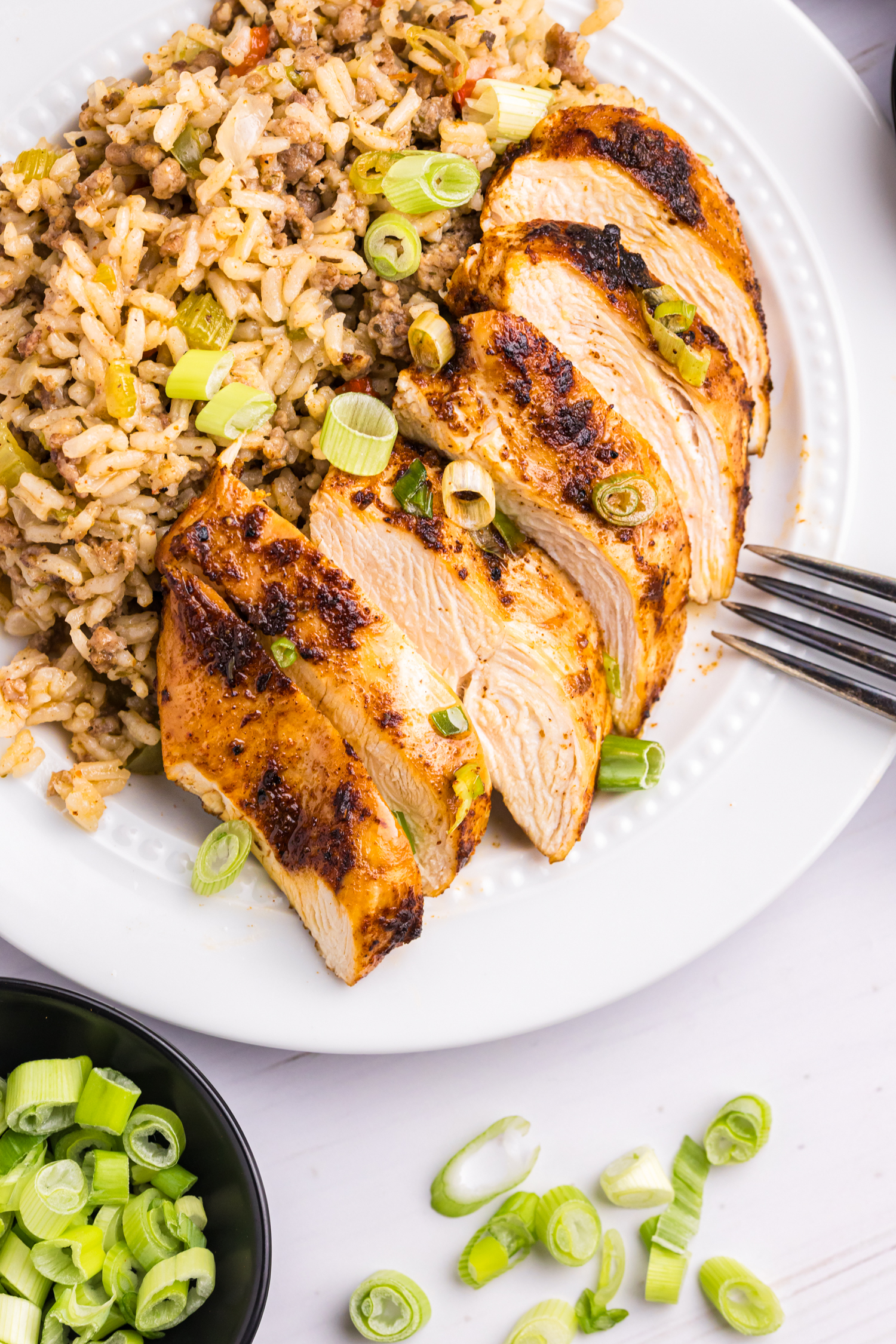 Sliced blackened chicken breast served on a plate next to a scoop of dirty rice, garnished with chopped green onions.