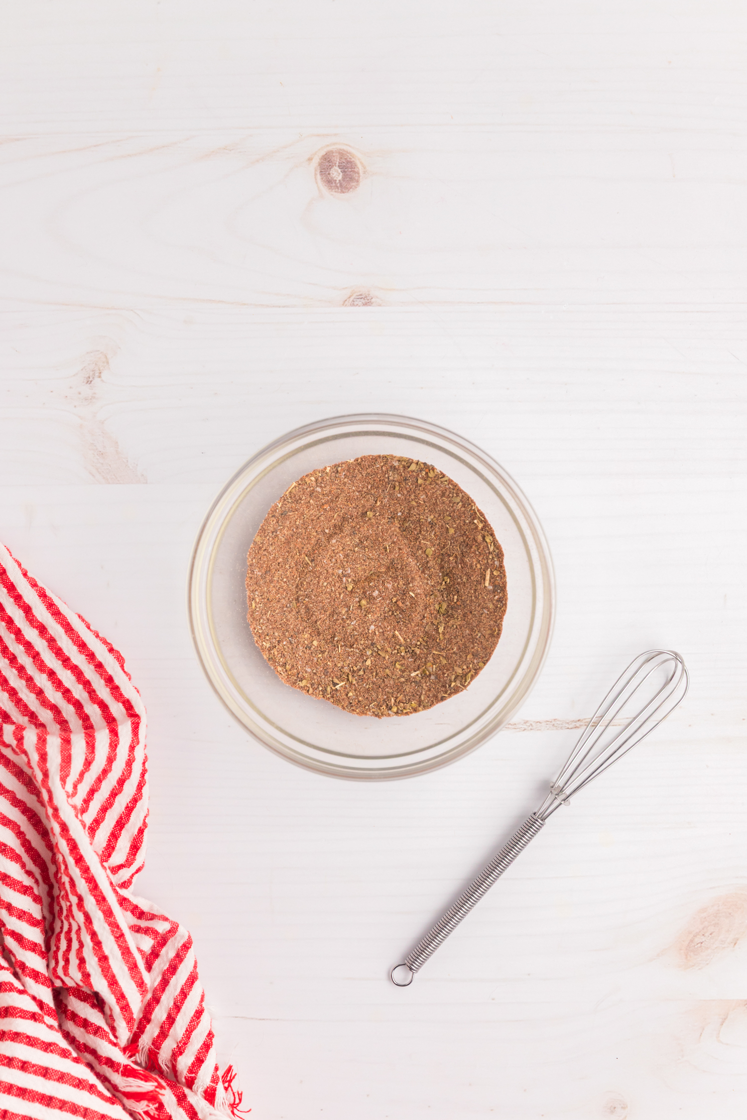 A glass bowl filled with thoroughly mixed blackened seasoning blend, placed on a white wooden surface.