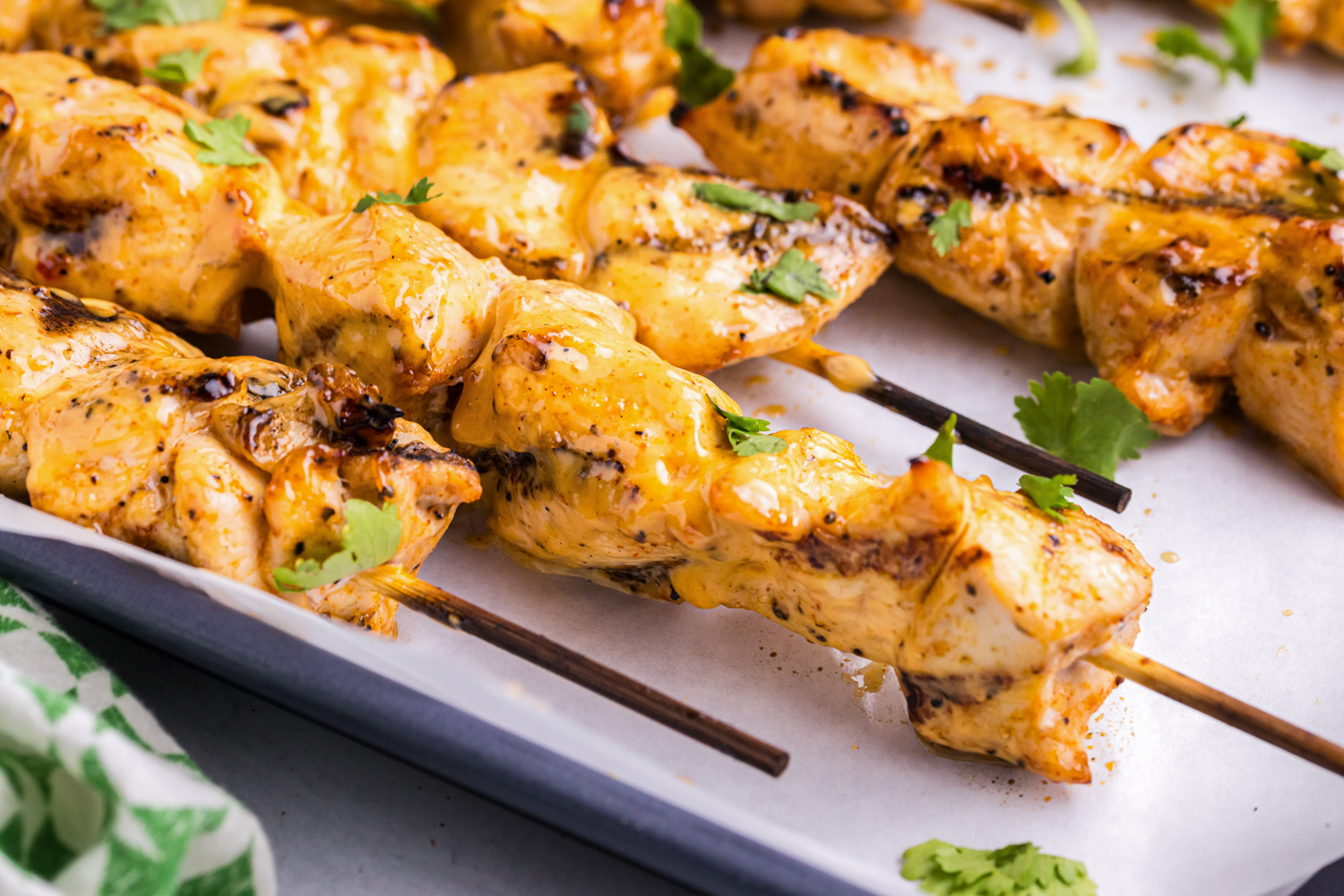 Close-up of grilled Bang Bang chicken skewers on a tray, glistening with sauce and topped with fresh cilantro leaves.