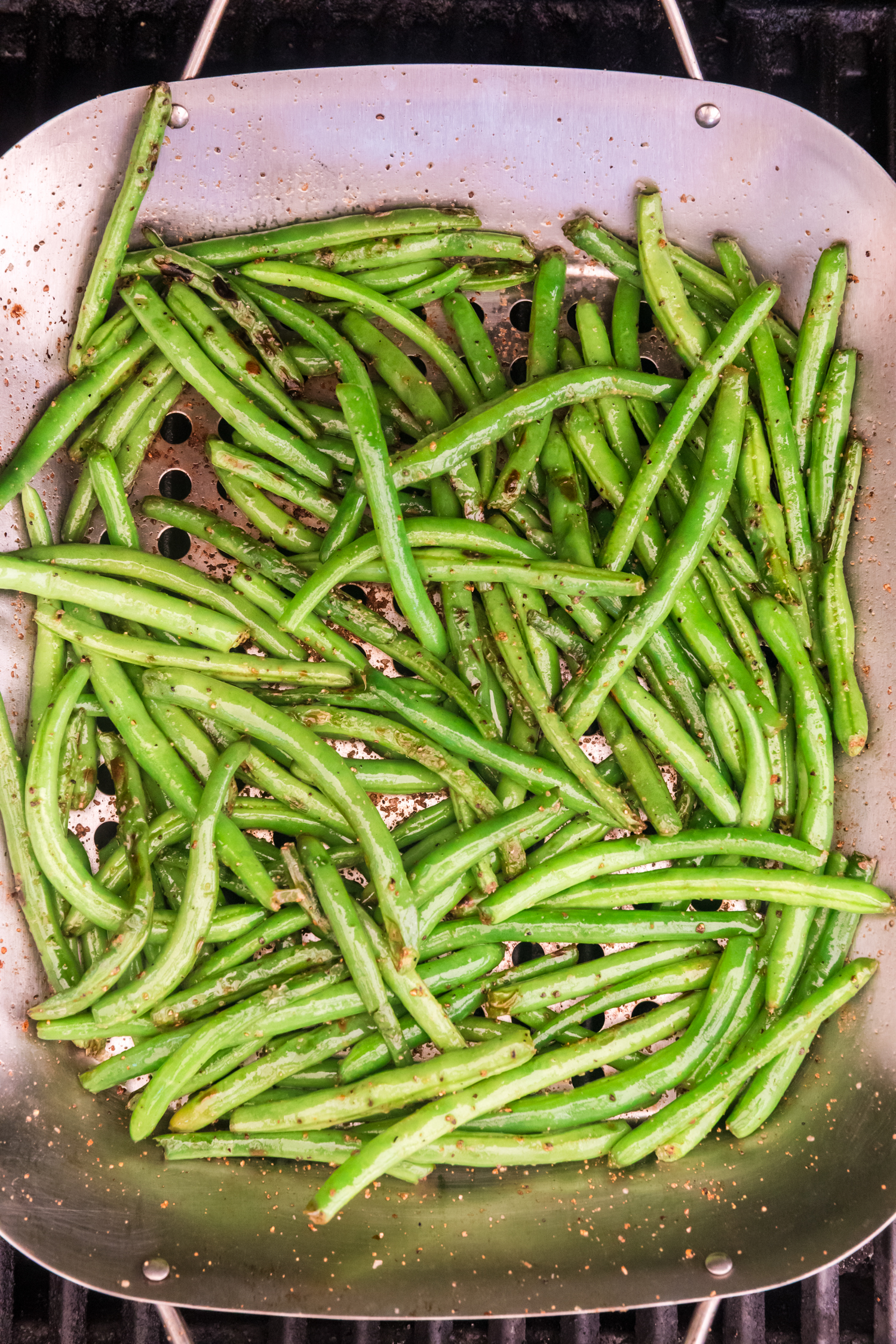 A wide view of a grilling basket filled with green beans being cooked over an open flame.