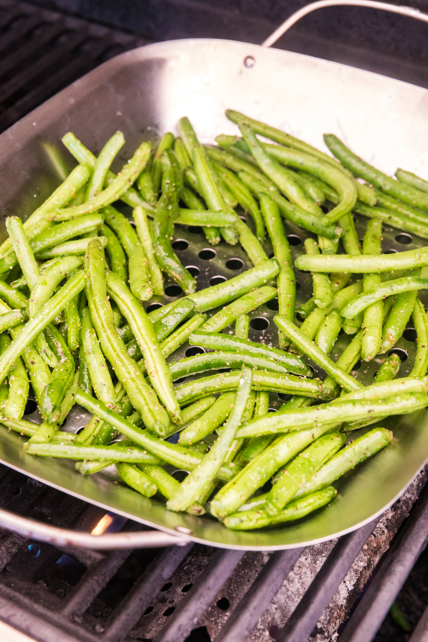 Seasoned green beans cooking in a grill basket on a barbecue, showing slight browning.