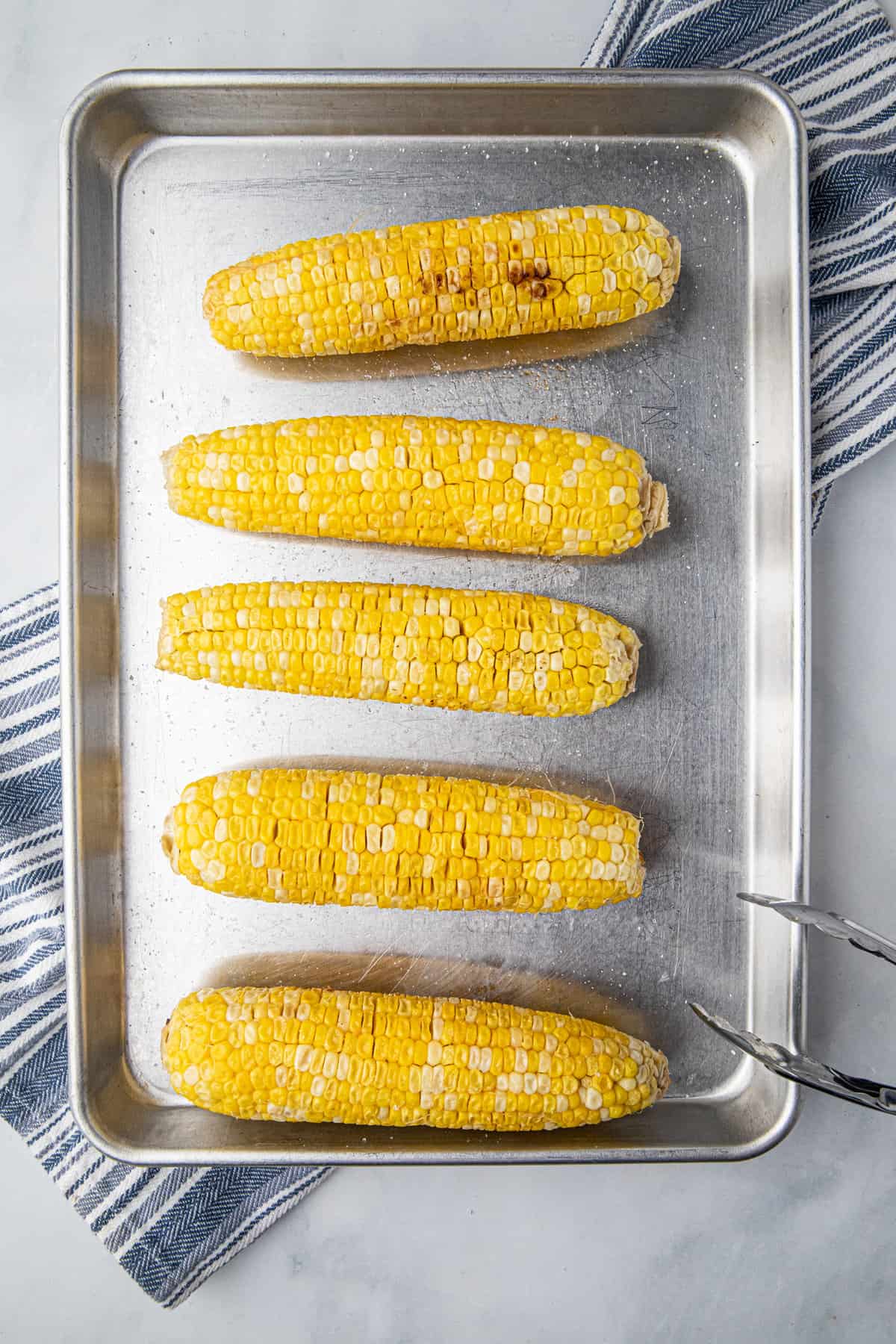 Smoked Corn on the Cob hot off the smoker on cooking sheet with tongs