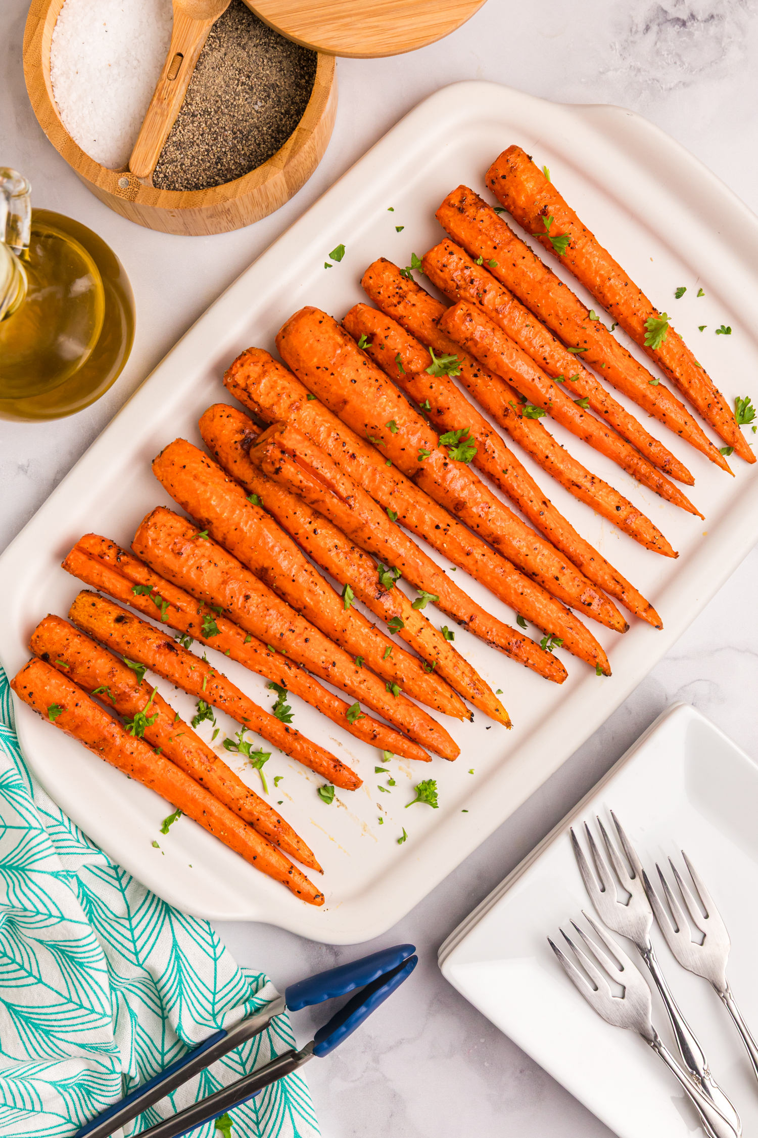 Grilled carrots garnished with chopped parsley and coarse salt, presented on a platter.