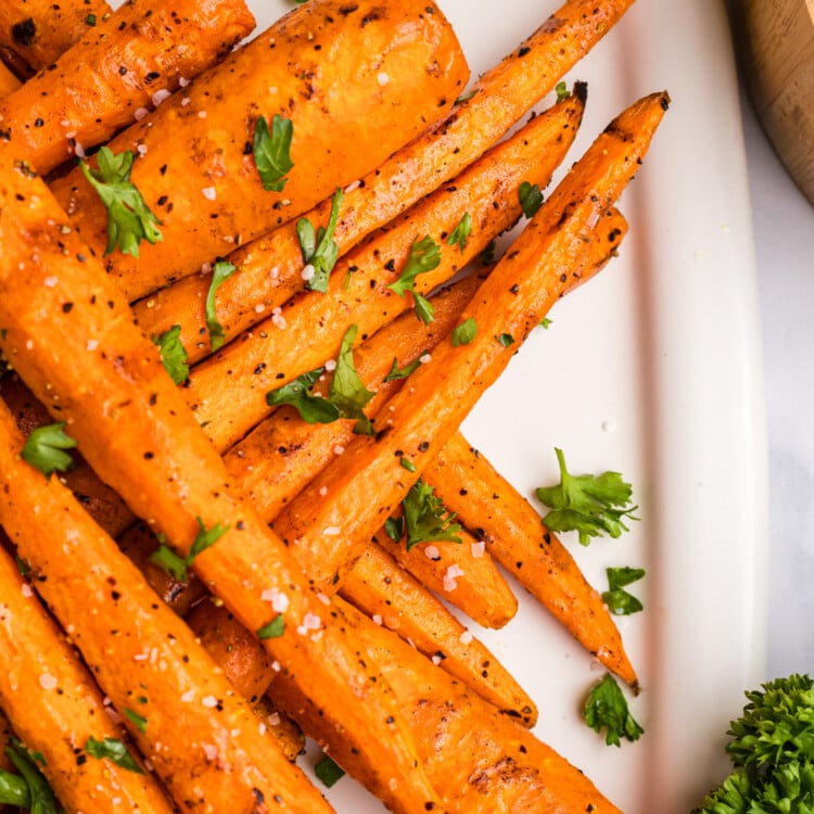 Close-up of a stacked pile of grilled carrots on a platter, garnished with parsley and sea salt.