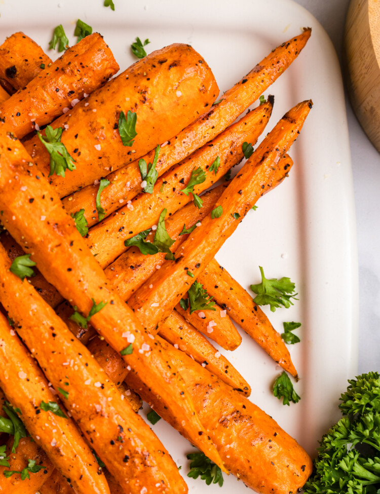Close-up of a stacked pile of grilled carrots on a platter, garnished with parsley and sea salt.