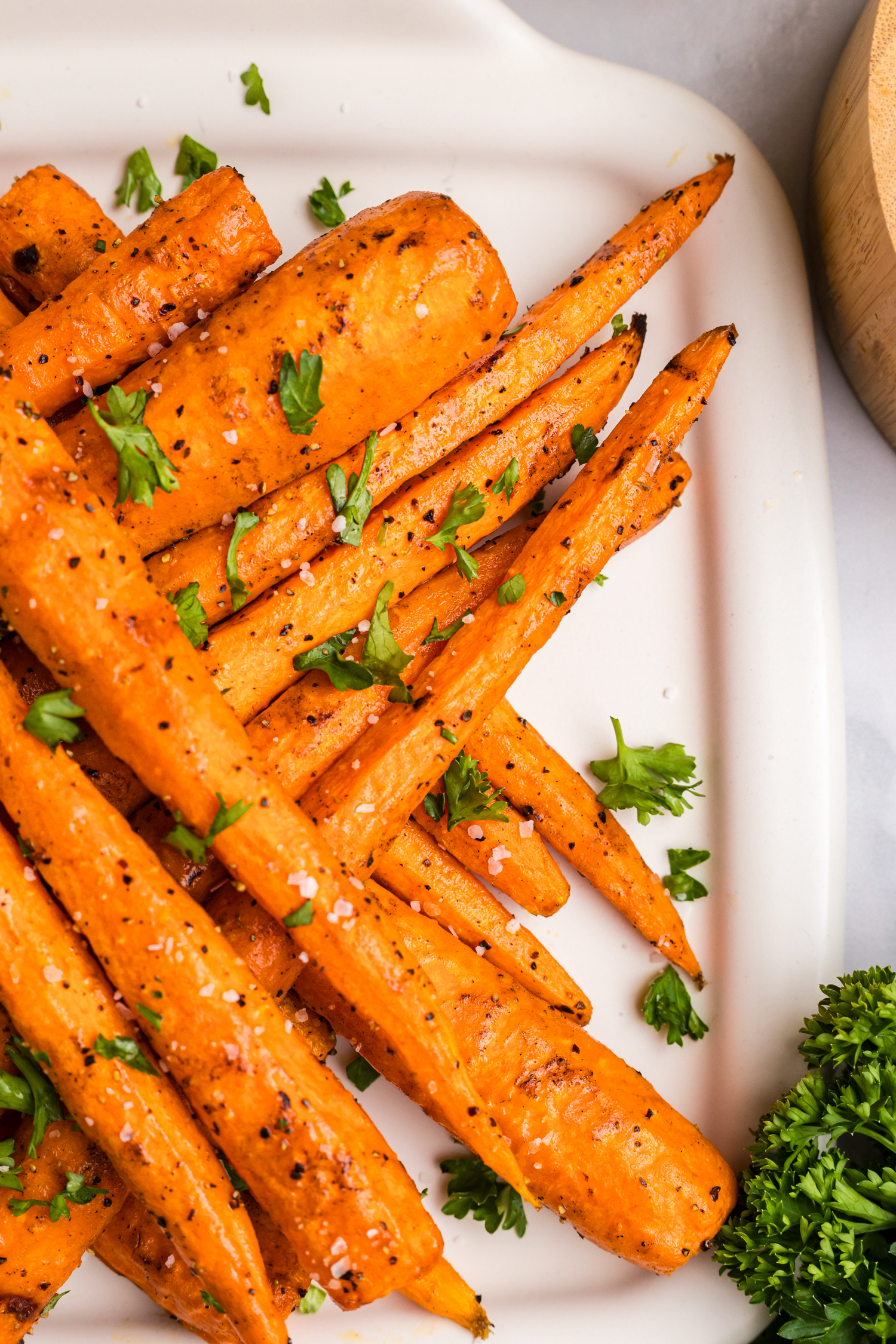 Close-up of a stacked pile of grilled carrots on a platter, garnished with parsley and sea salt.