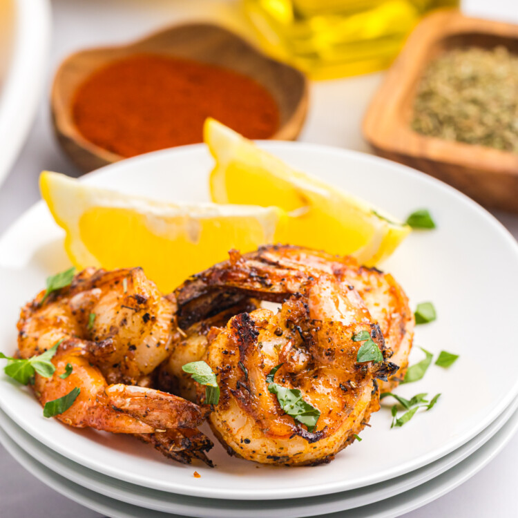 Close-up of grilled shrimp served on a white plate with lemon wedges and garnished with chopped parsley.