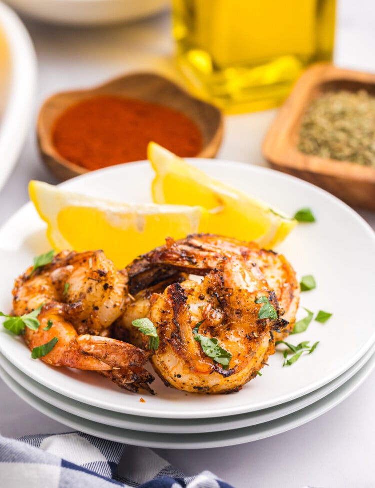 Close-up of grilled shrimp served on a white plate with lemon wedges and garnished with chopped parsley.