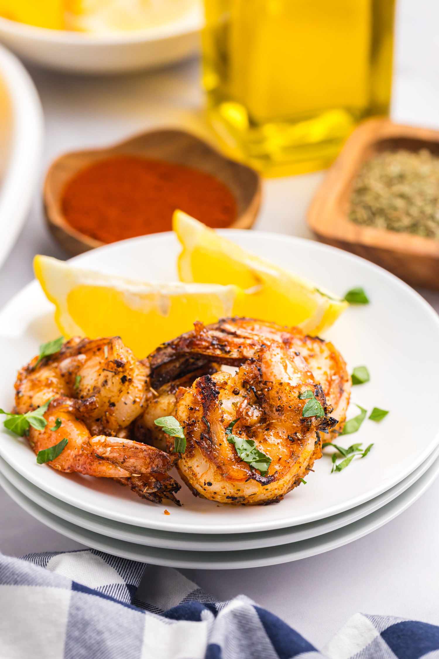 Close-up of grilled shrimp served on a white plate with lemon wedges and garnished with chopped parsley.

