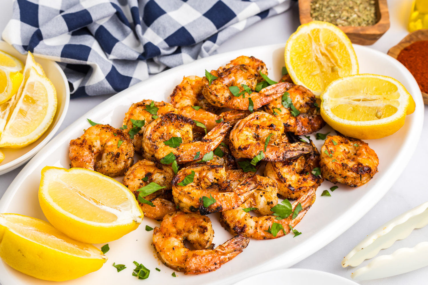Final plated presentation of grilled shrimp on a white platter, garnished with fresh parsley and surrounded by lemon wedges.