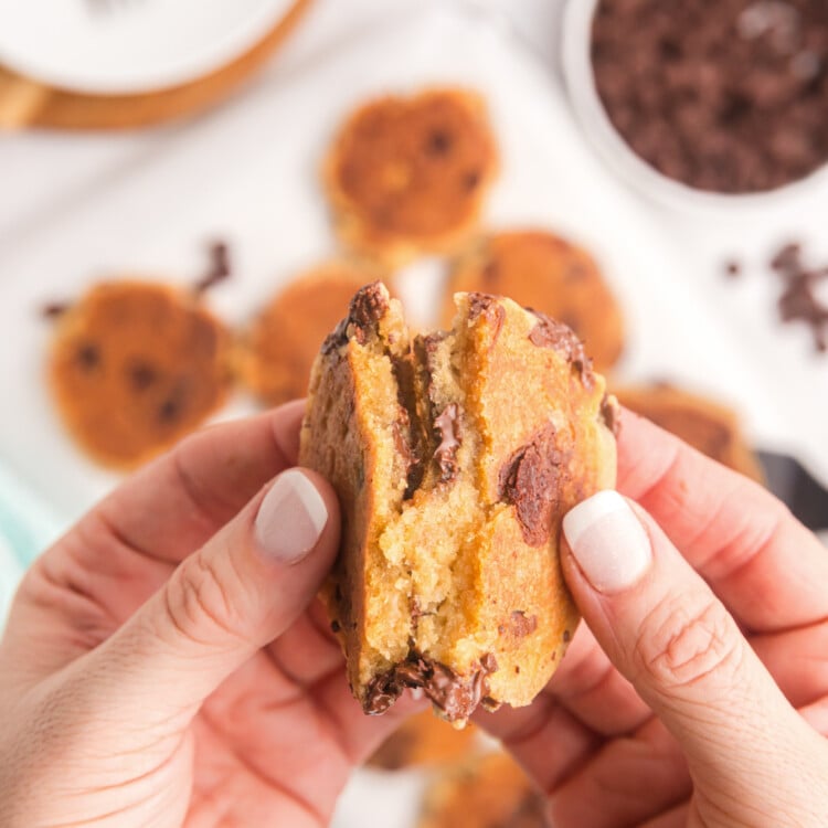 A pair of hands pulling apart a freshly cooked chocolate chip cookie, revealing a warm, gooey center with melted chocolate chips.