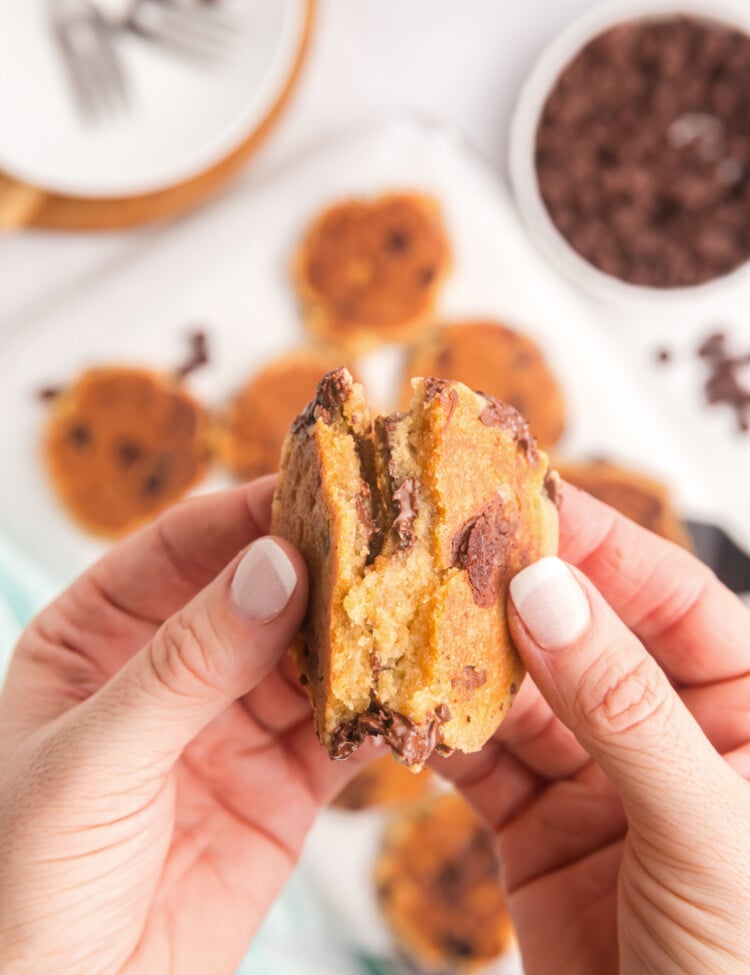 A pair of hands pulling apart a freshly cooked chocolate chip cookie, revealing a warm, gooey center with melted chocolate chips.