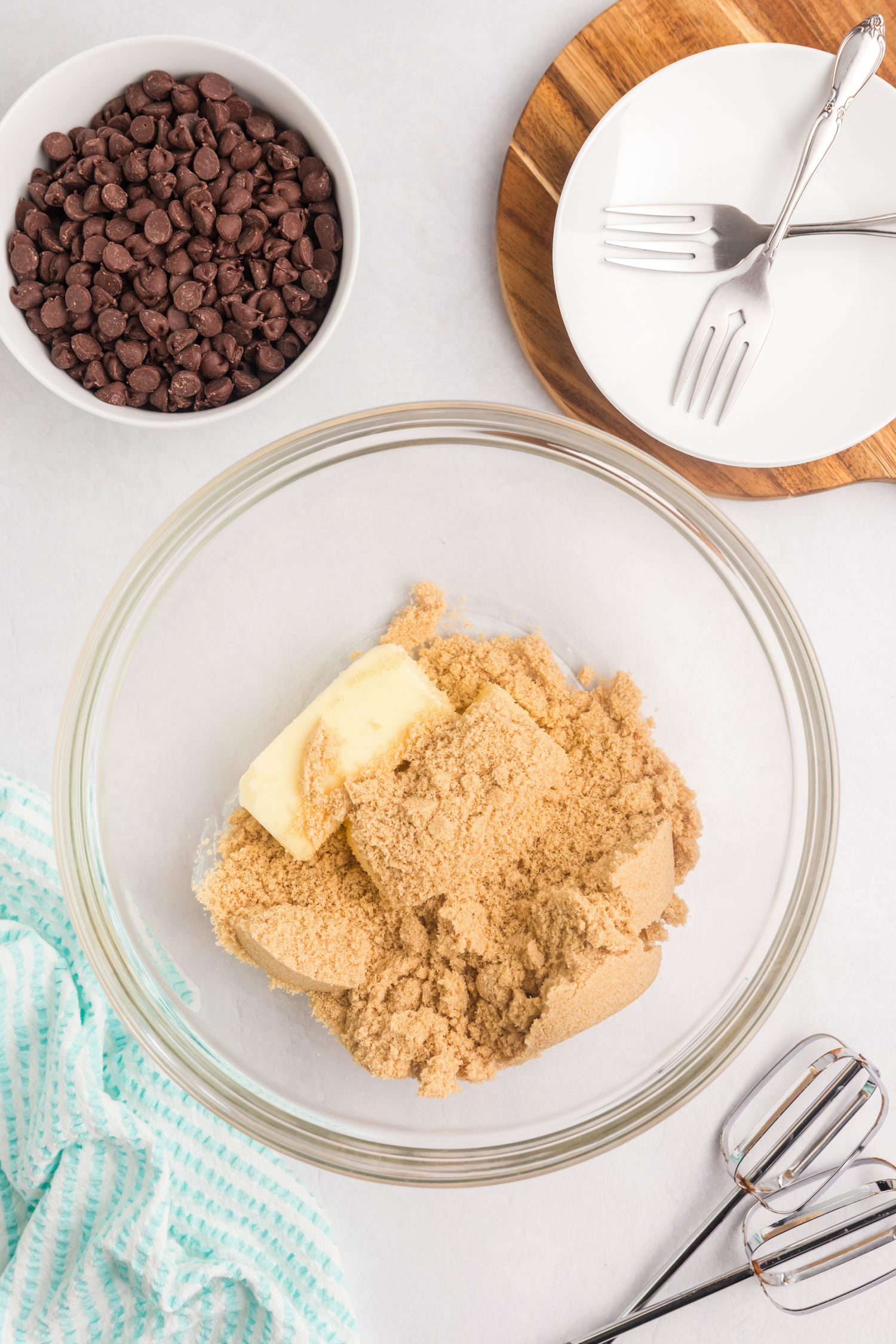A glass mixing bowl with softened butter and packed brown sugar, ready to be creamed. An electric beater is placed beside the bowl.