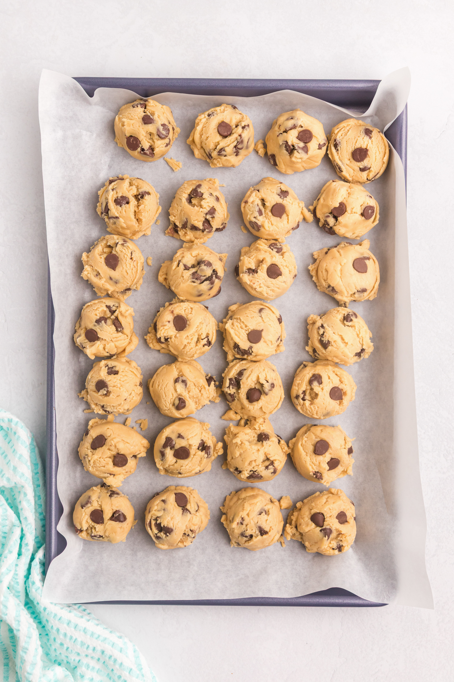 Dough balls of chocolate chip cookie dough are neatly portioned onto a parchment-lined baking tray, ready to be baked.