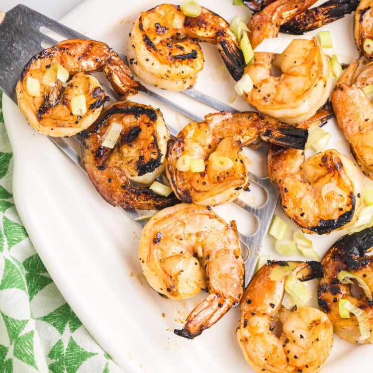 Close-up of grilled shrimp served on a white platter with metal skewers, garnished with chopped green onions and slightly charred edges, ready to eat.