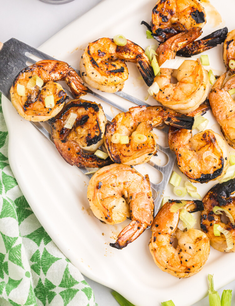Close-up of grilled shrimp served on a white platter with metal skewers, garnished with chopped green onions and slightly charred edges, ready to eat.