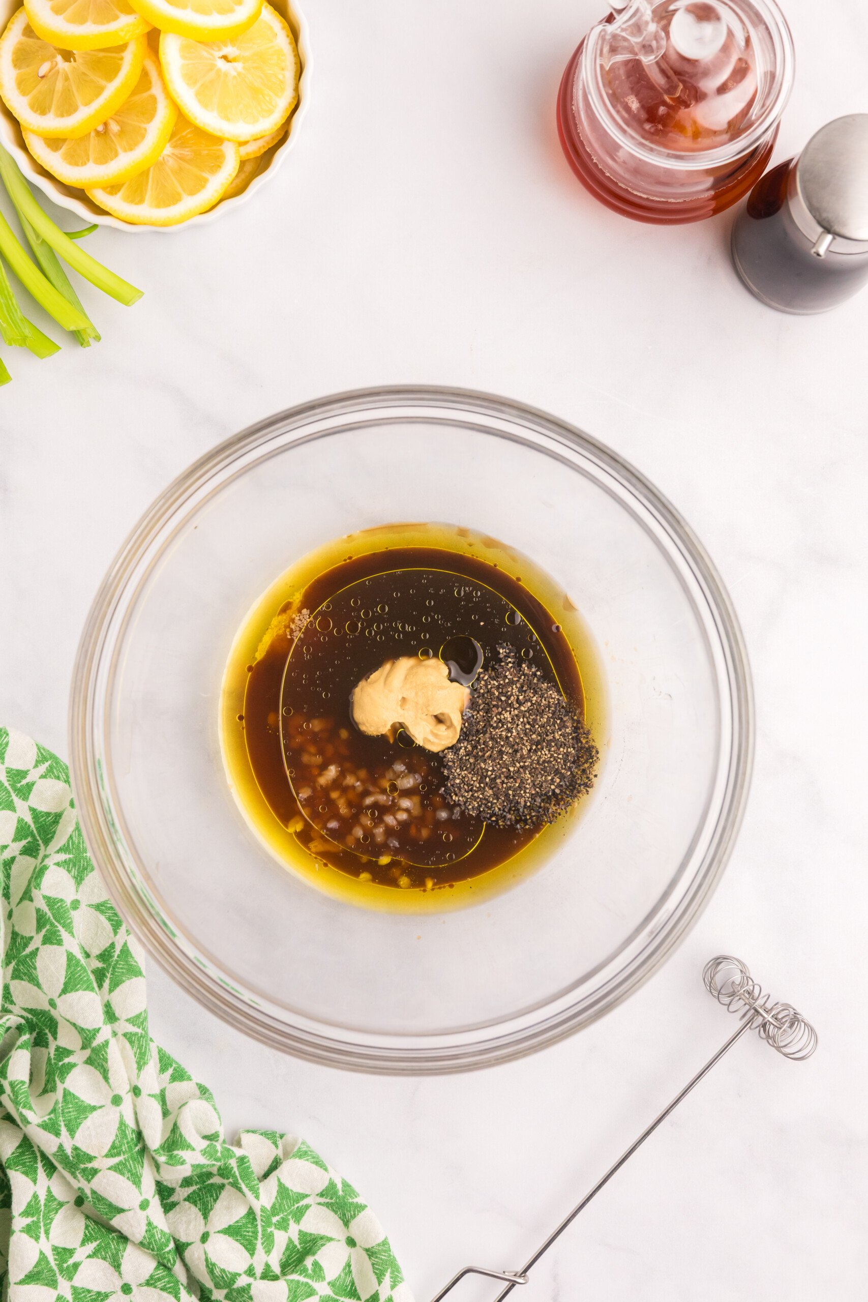 A mixing bowl with marinade ingredients including olive oil, soy sauce, Dijon mustard, black pepper, garlic, and possibly honey.