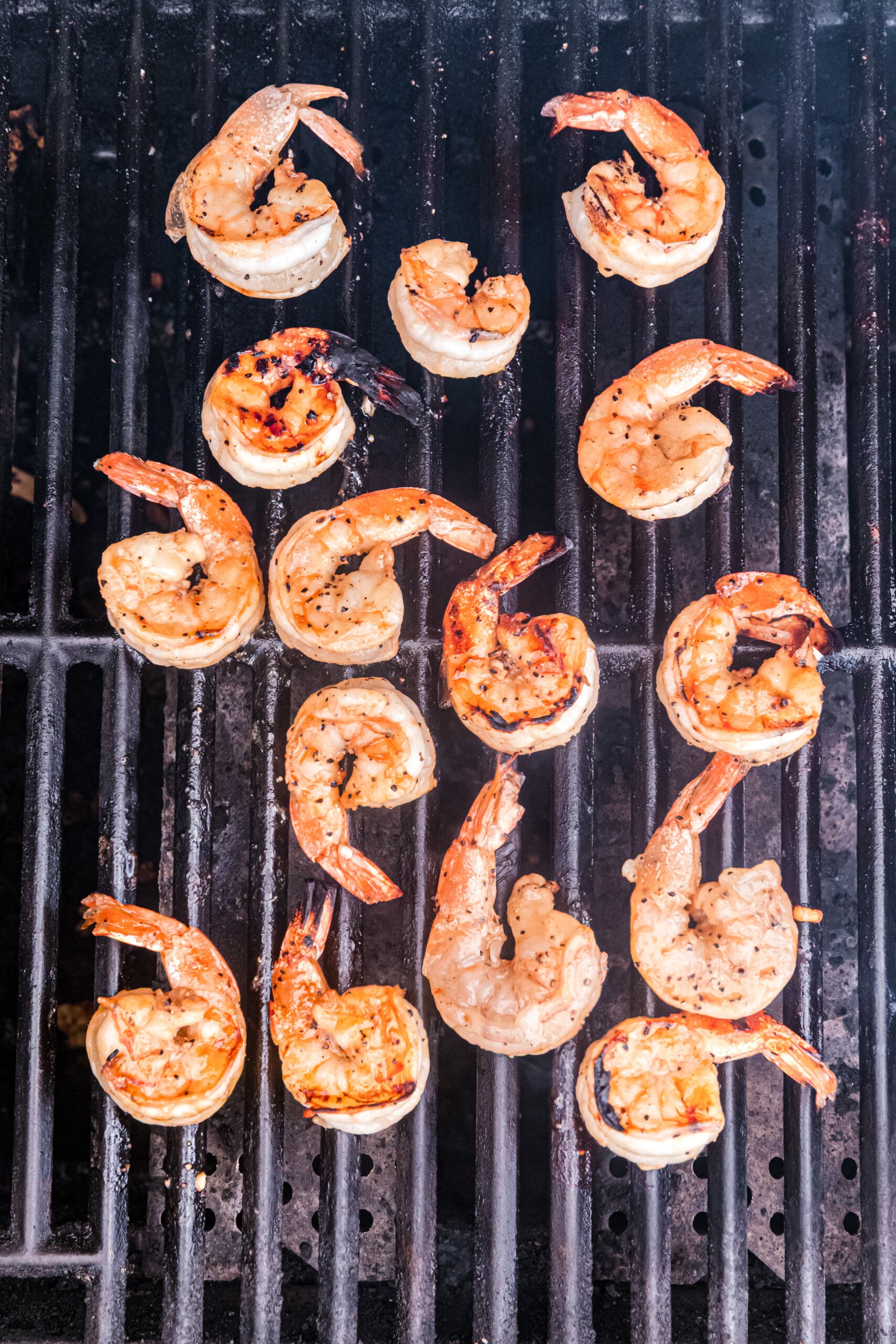 Shrimp flipped and continuing to grill, showing some char marks.